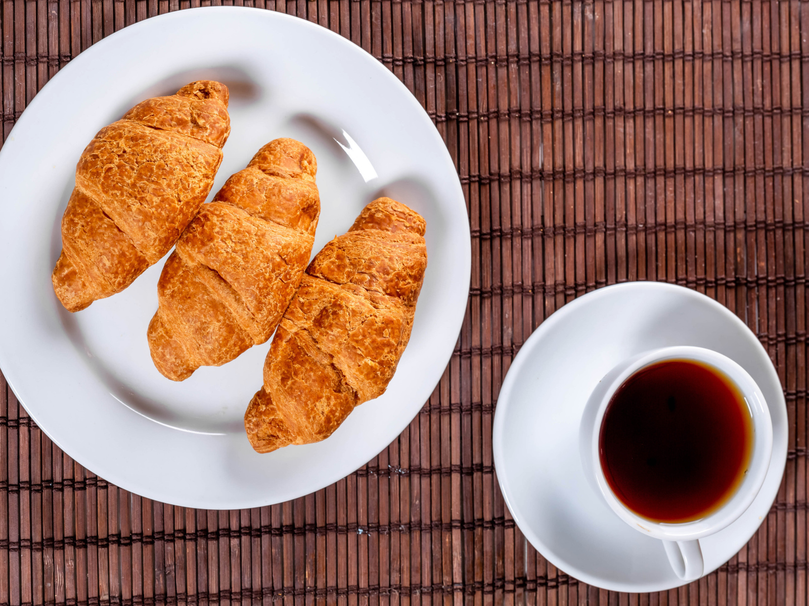 Three croissants on a white plate on a table with tea