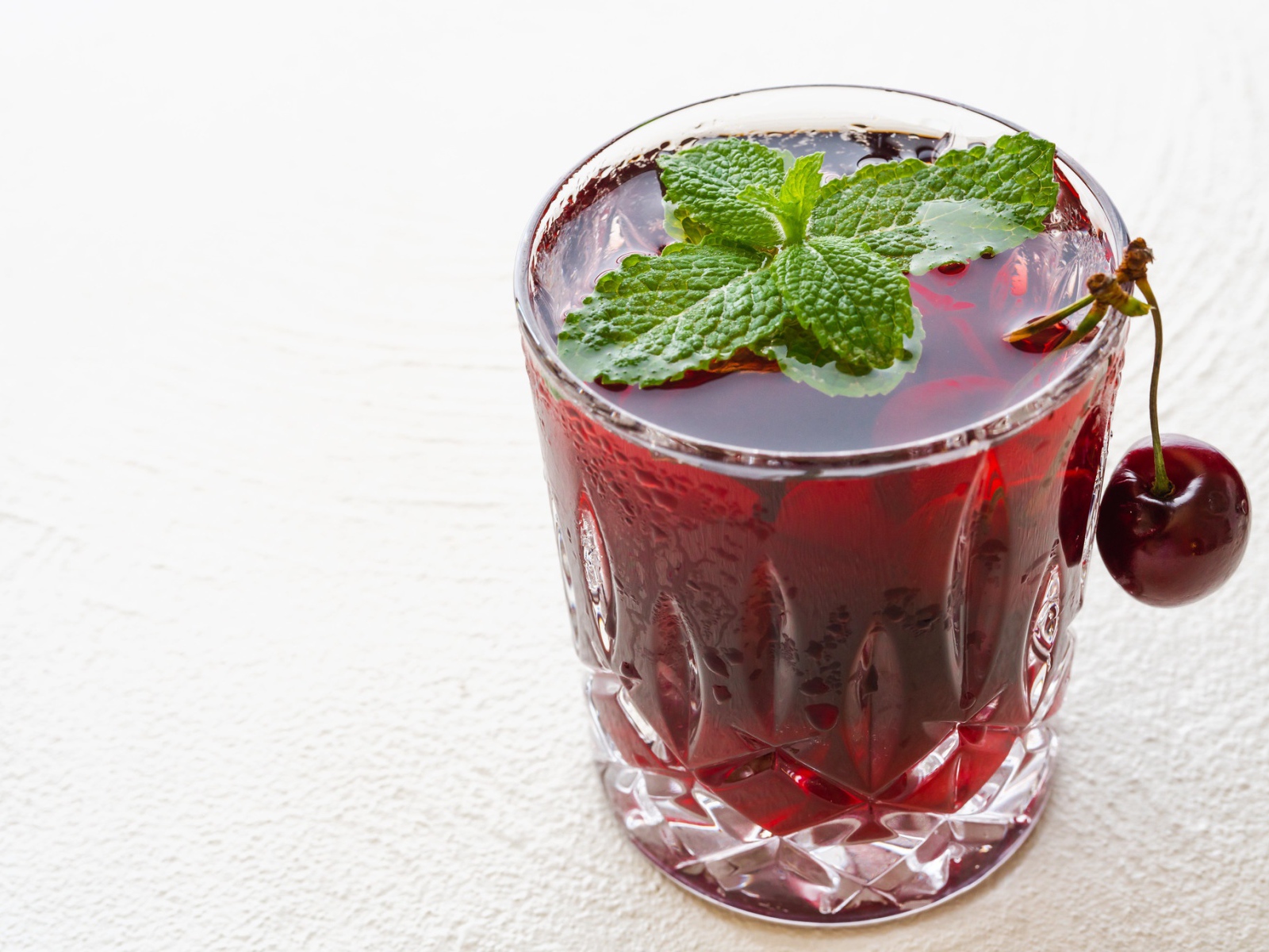 Стакан вишневого сока с мятой на белом фоне