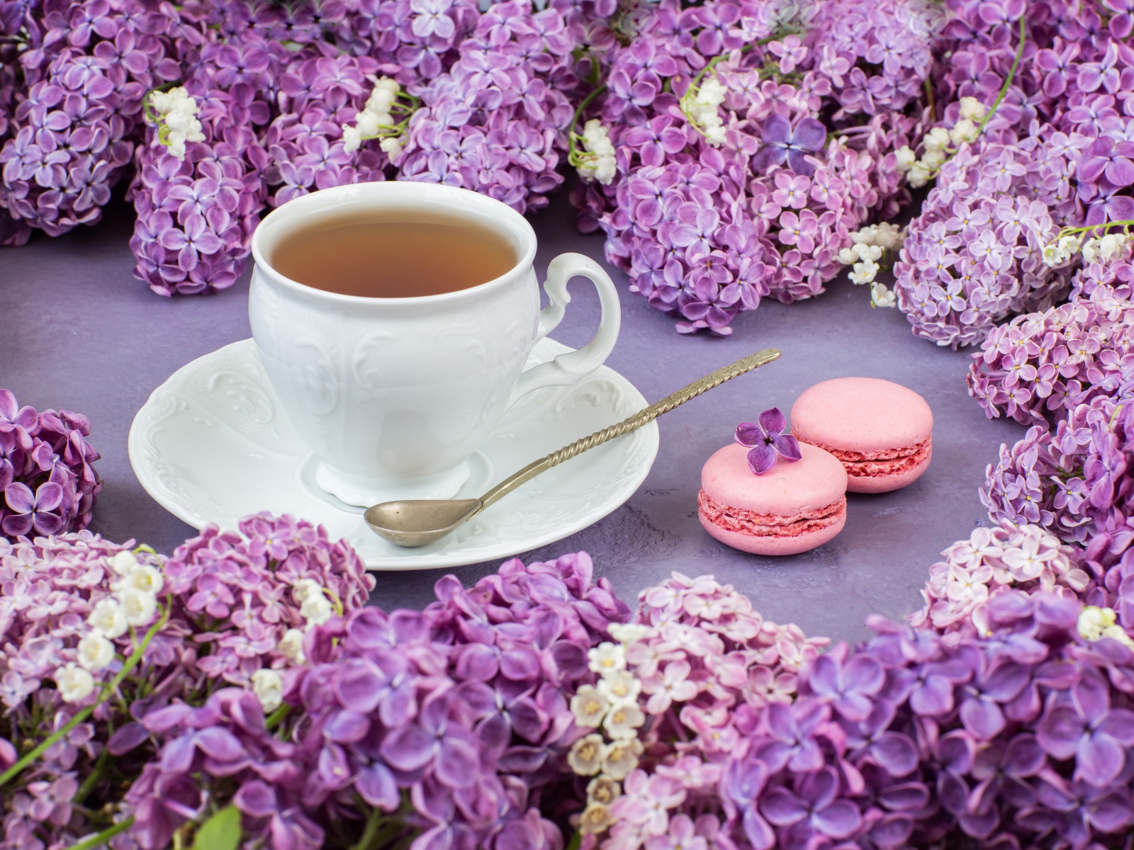 Чашка чая на столе с цветами сирени и десертом макарон