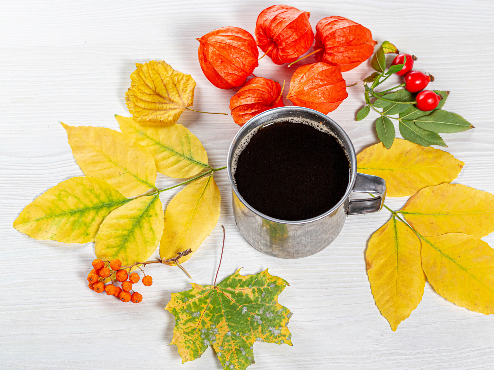Кружка кофе на столе с осенними листьями, физалисом и шиповником