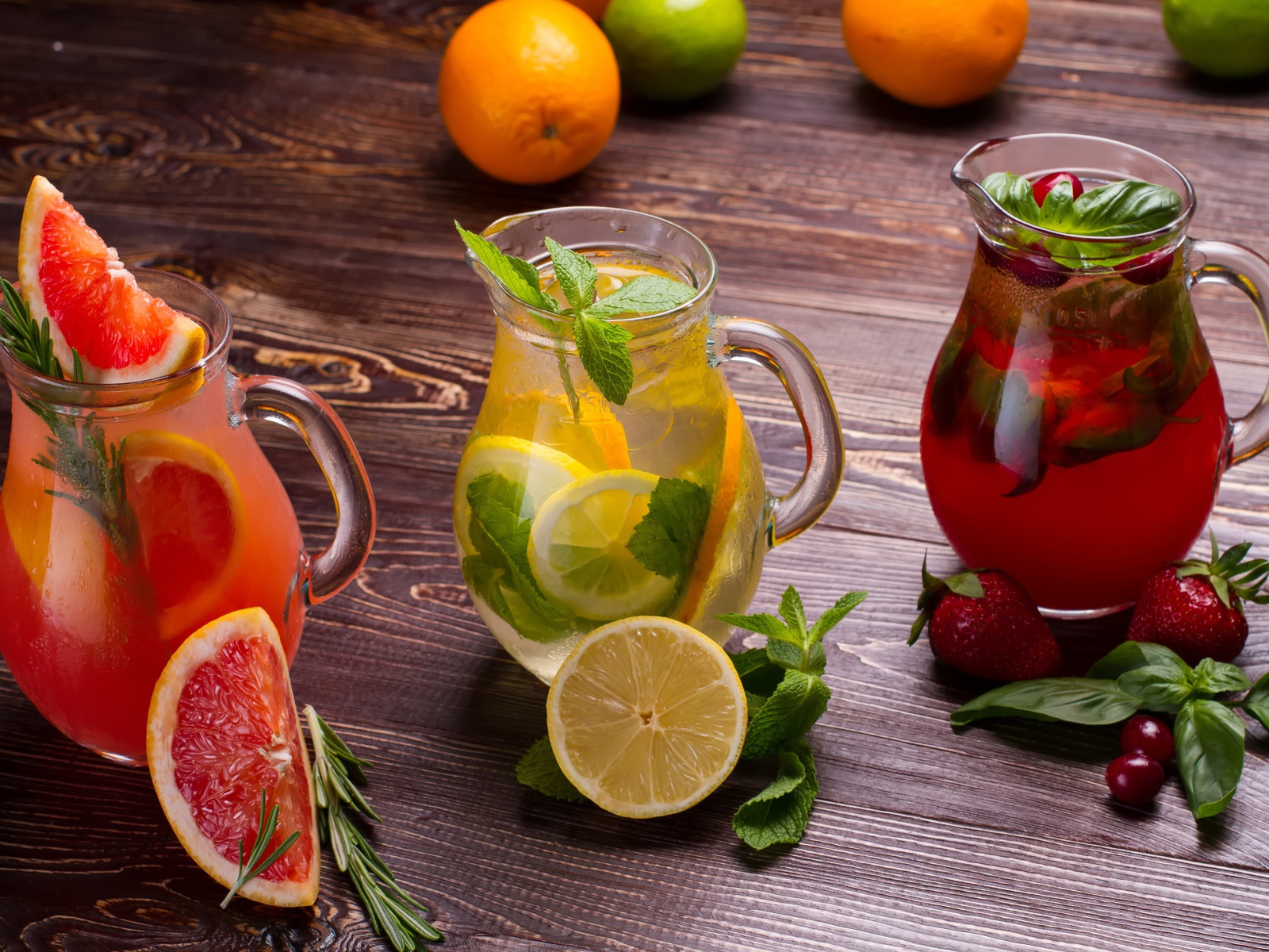 Три стеклянных графина с напитком на деревянном столе с фруктами