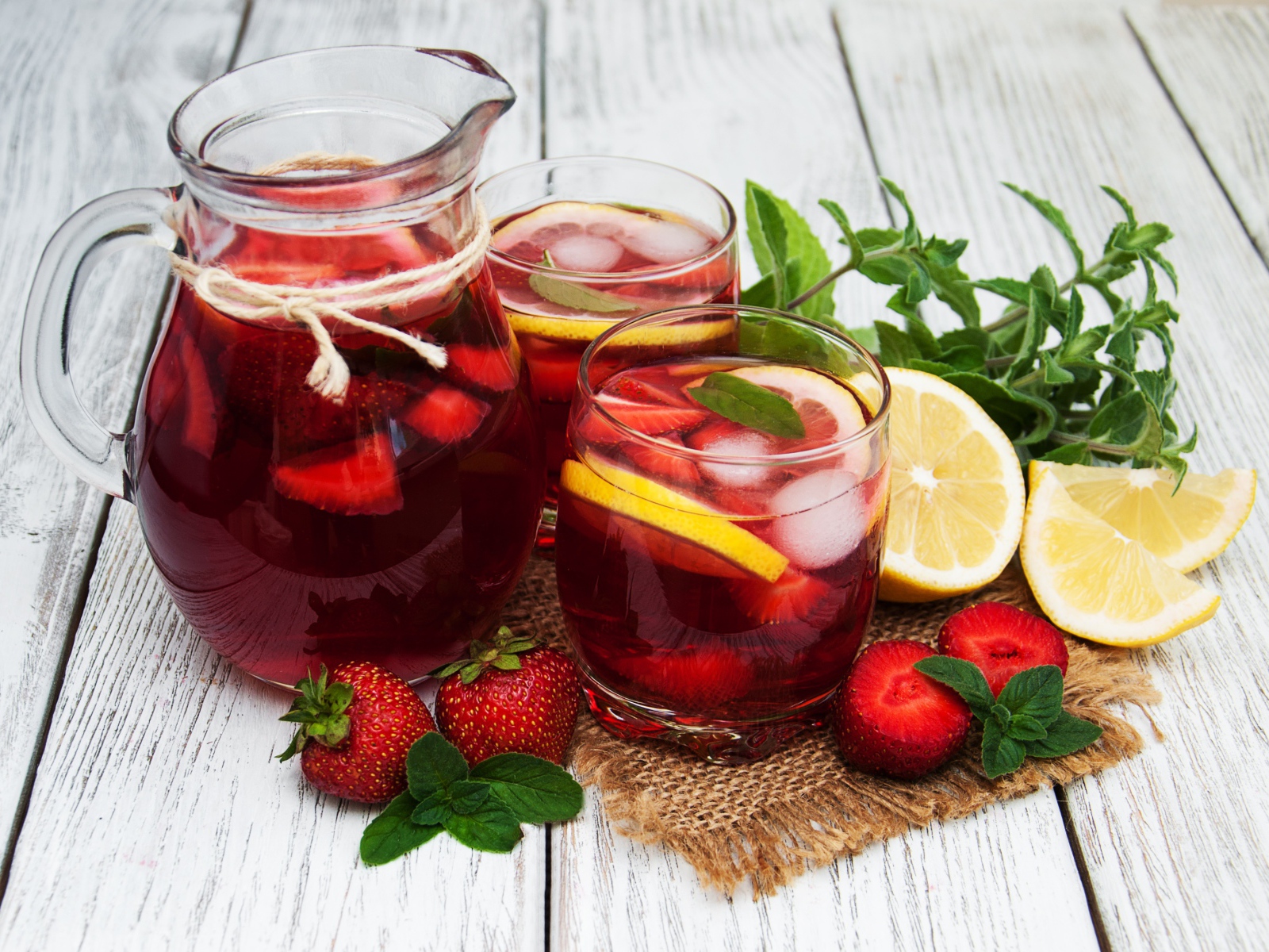 Два стакана мохито на столе с графином, лимоном, клубникой и мятой