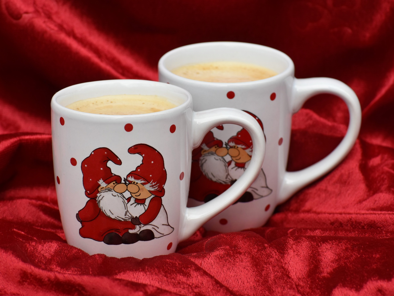 Две белые чашки кофе с рисунком стоят на красной ткани