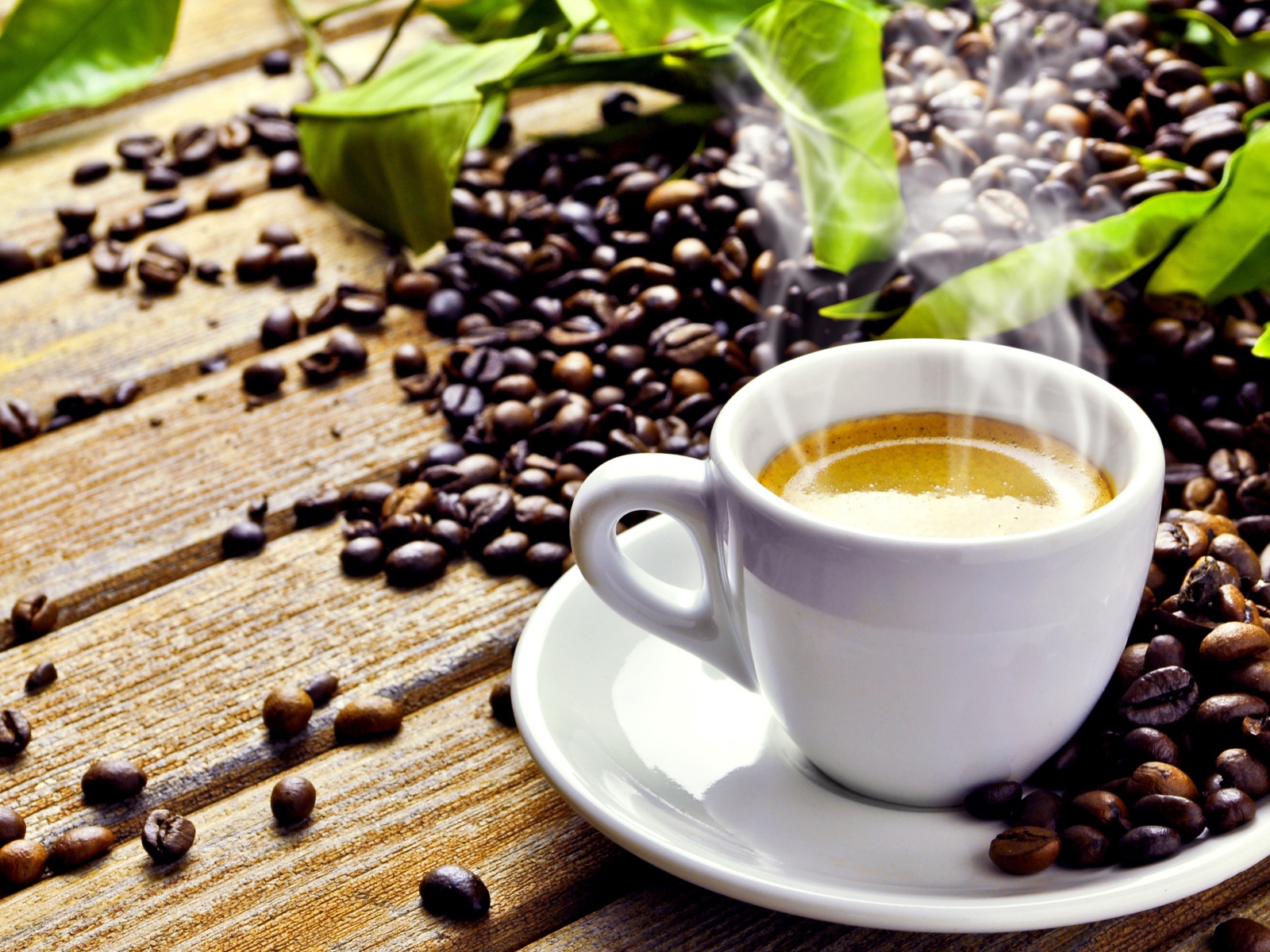 Белая чашка с горячим кофе на деревянном столе с кофейными зернами