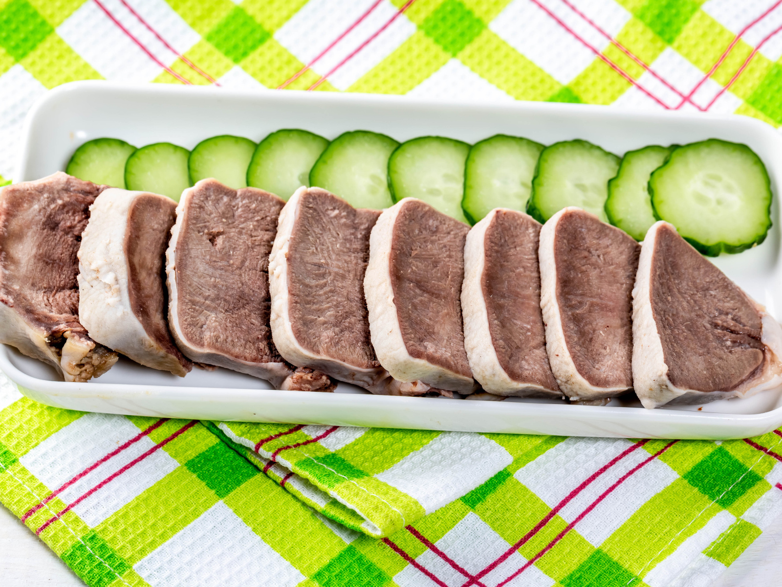 Вареный язык на тарелке со свежими огурцами