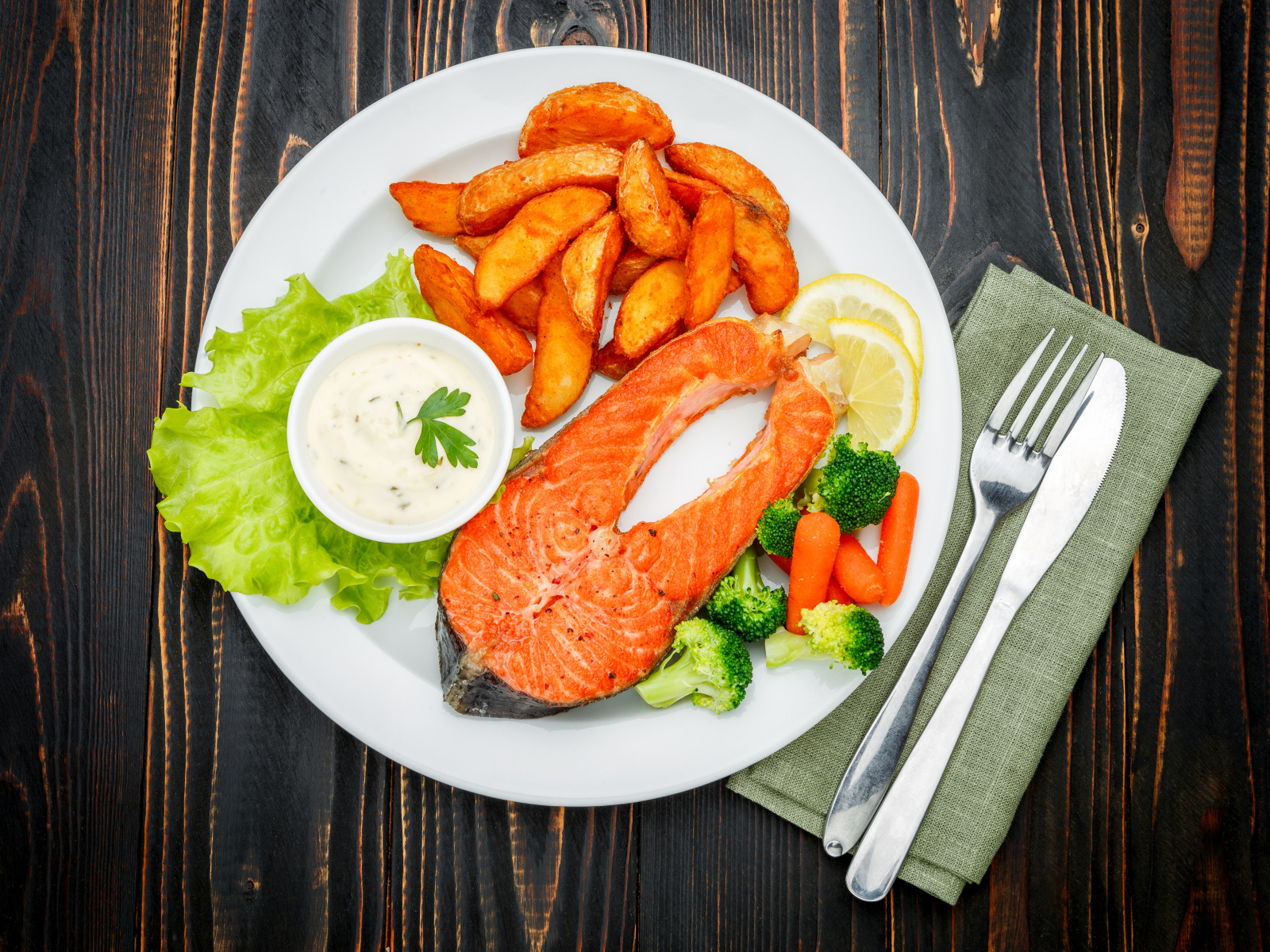 Кусок красной рыбы на тарелке с картофелем и соусом