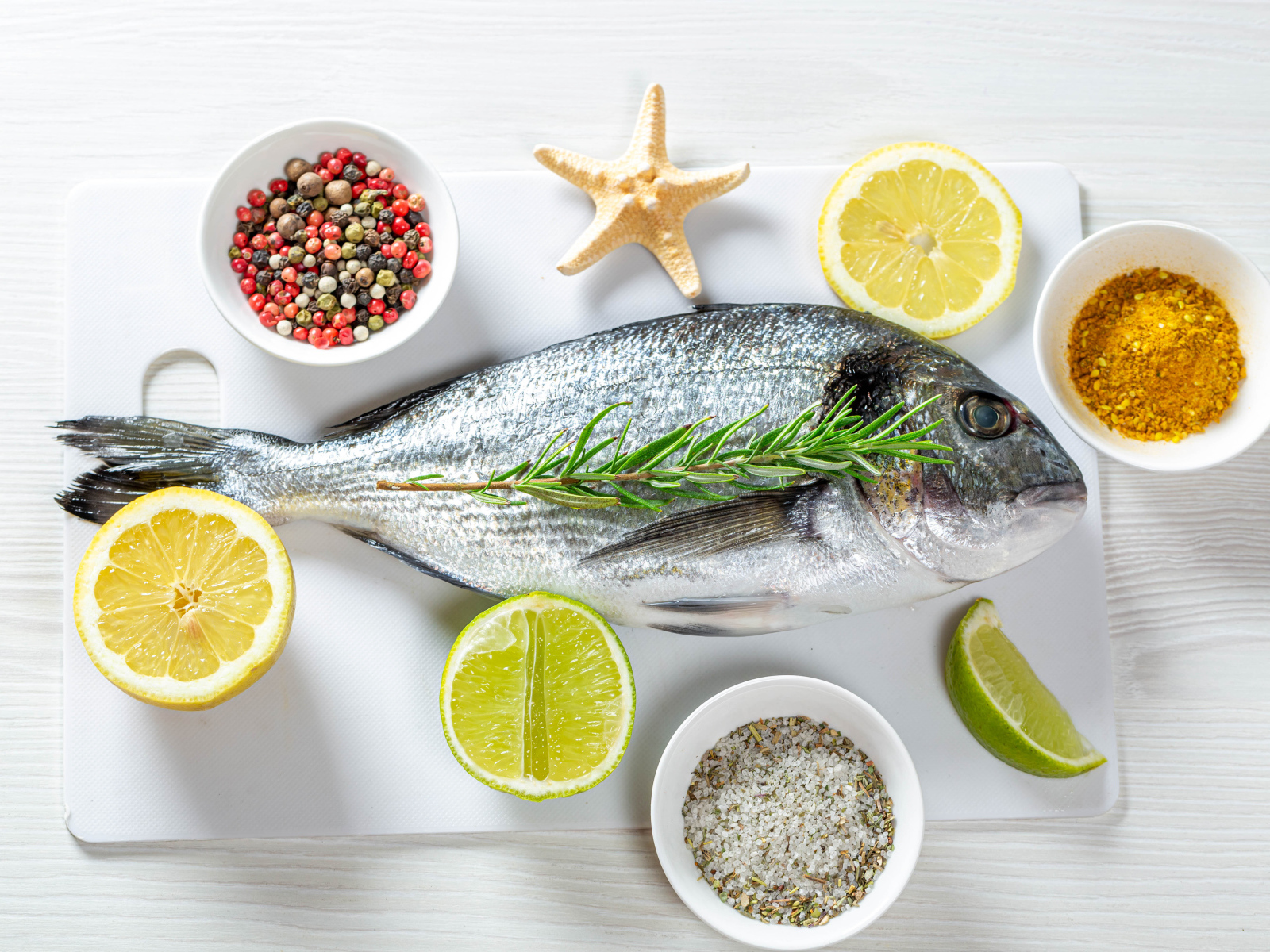 Свежая рыба на доске с солью, перцем, куркумой и лимоном