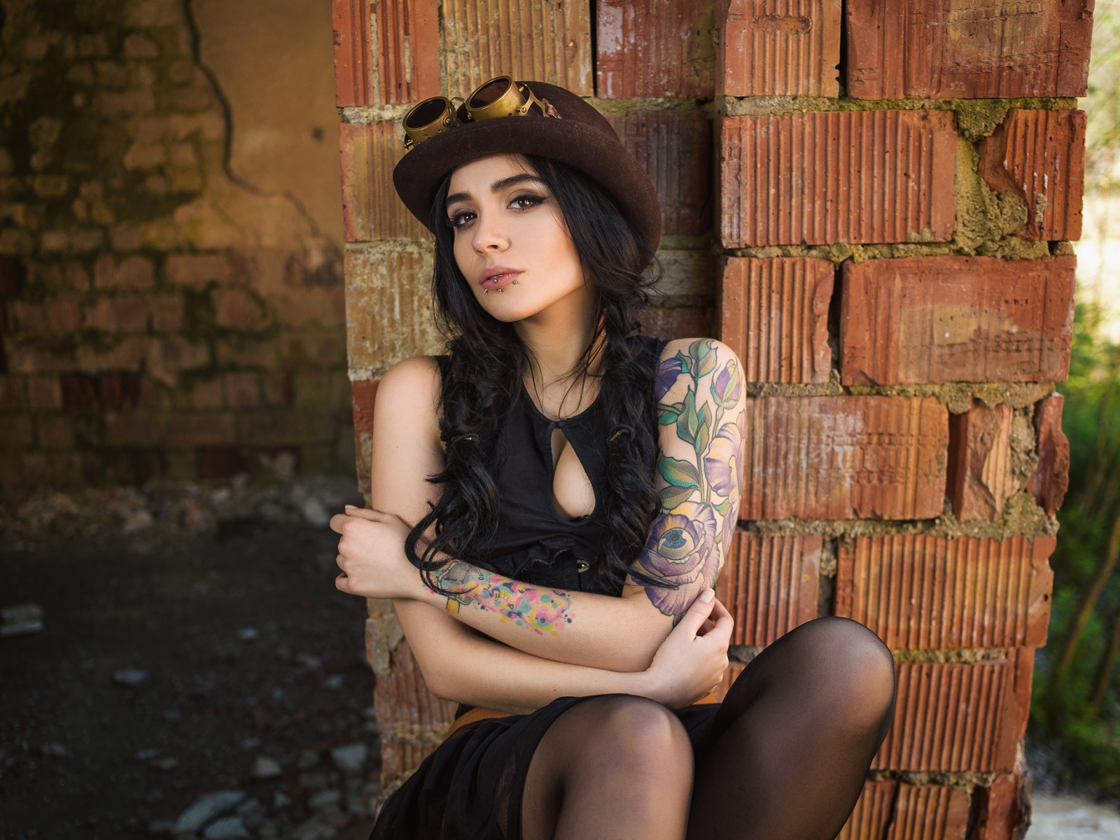 The girl in a hat with tattoos on his arm sits near the wall