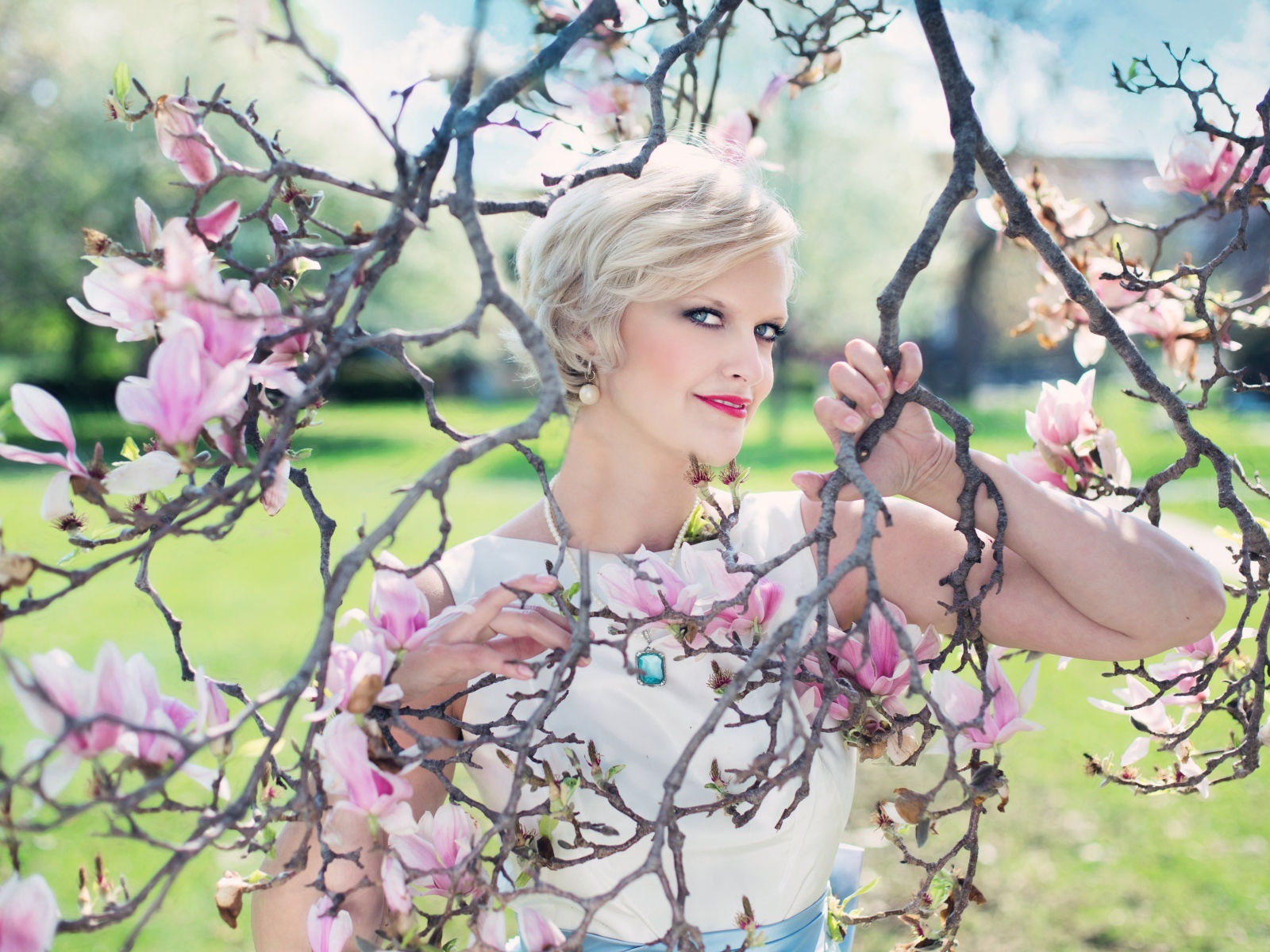 Красивая женщина с короткой стрижкой стоит у цветущей магнолии 