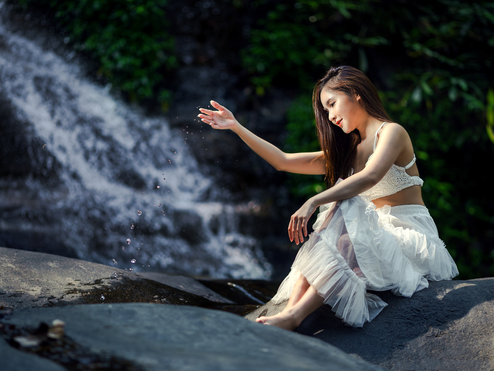 Красивая девушка азиатка в белом платье сидит у воды