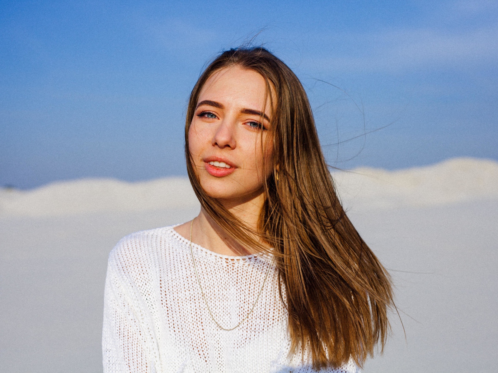 Красивая голубоглазая девушка в белом свитере на фоне голубого неба