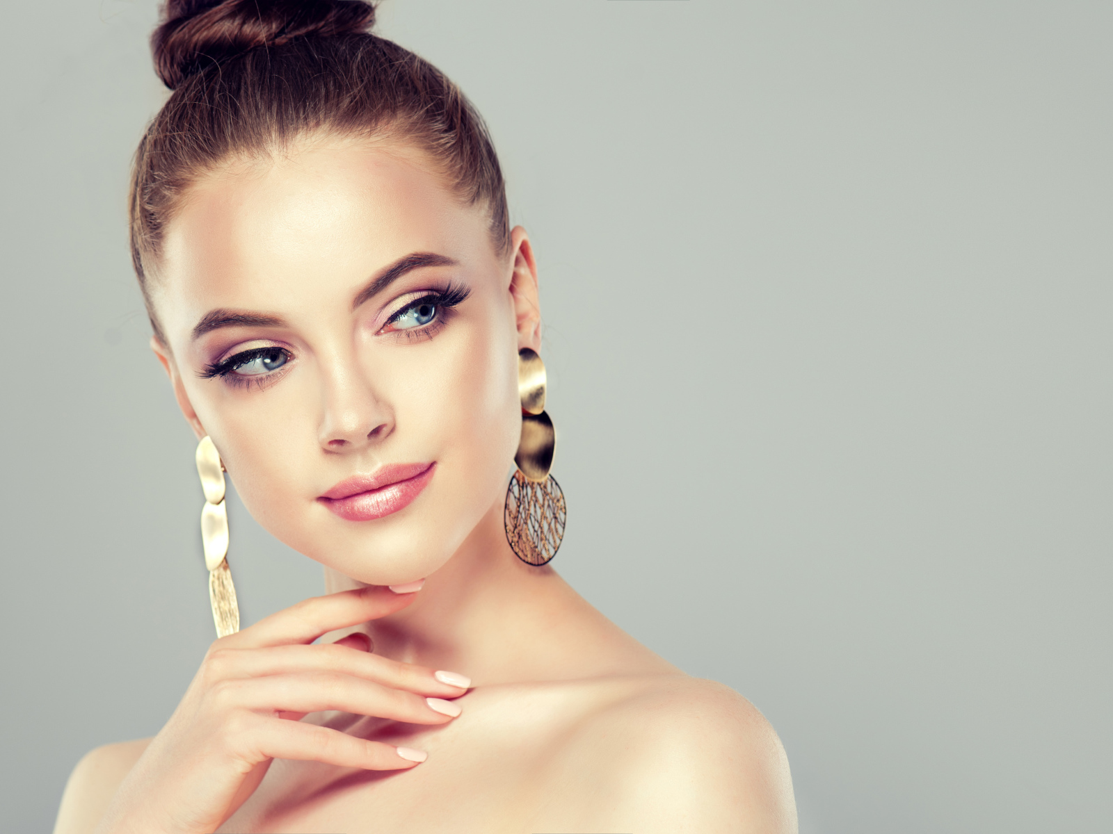 Красивая девушка шатенка с золотыми серьгами в ушах на сером фоне