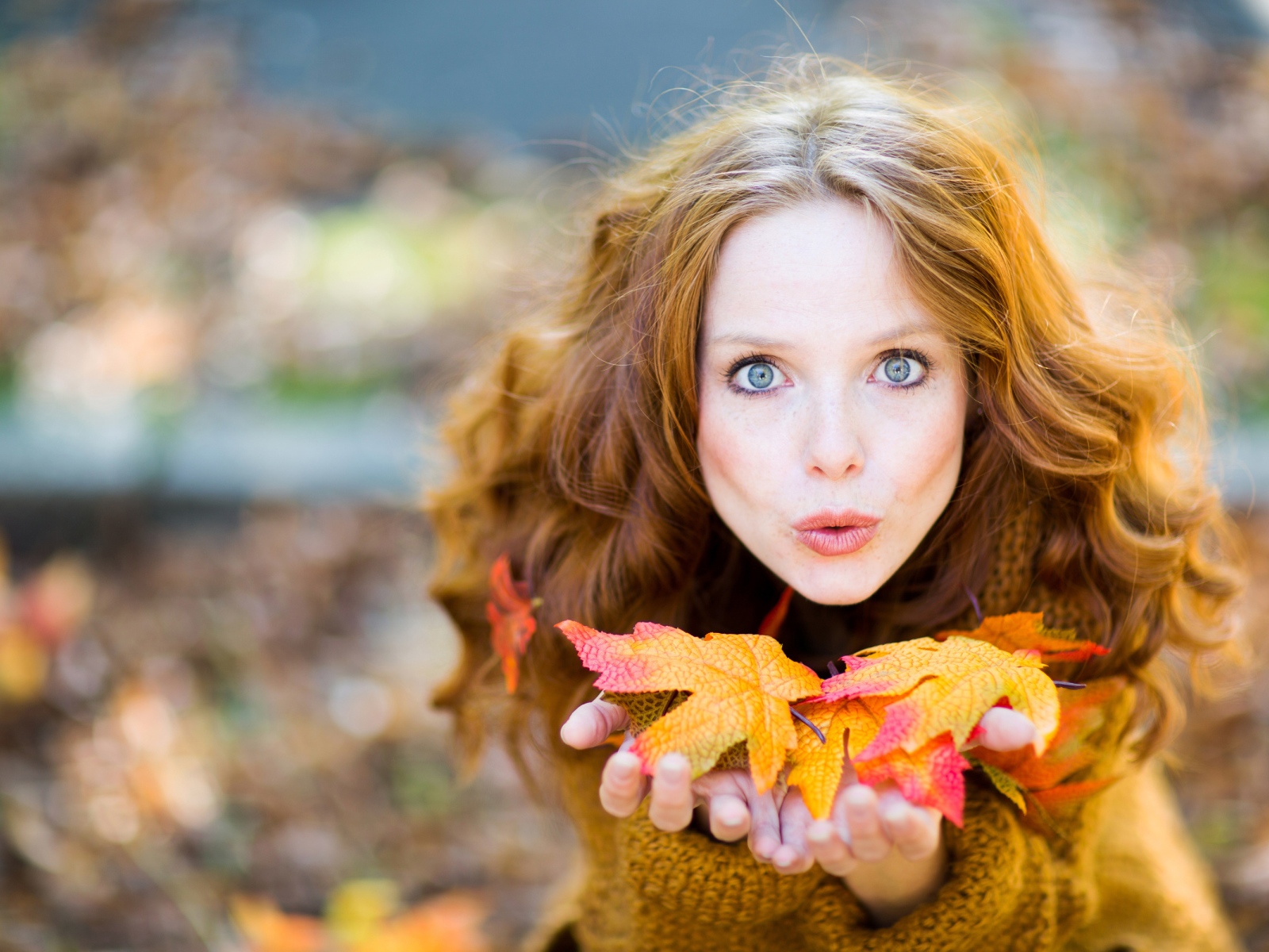 Красивая девушка сдувает листья с ладоней