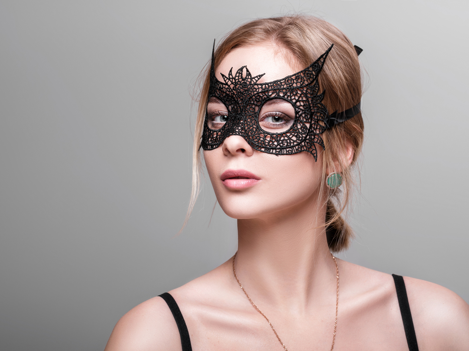 Красивая девушка в черной маске на сером фоне