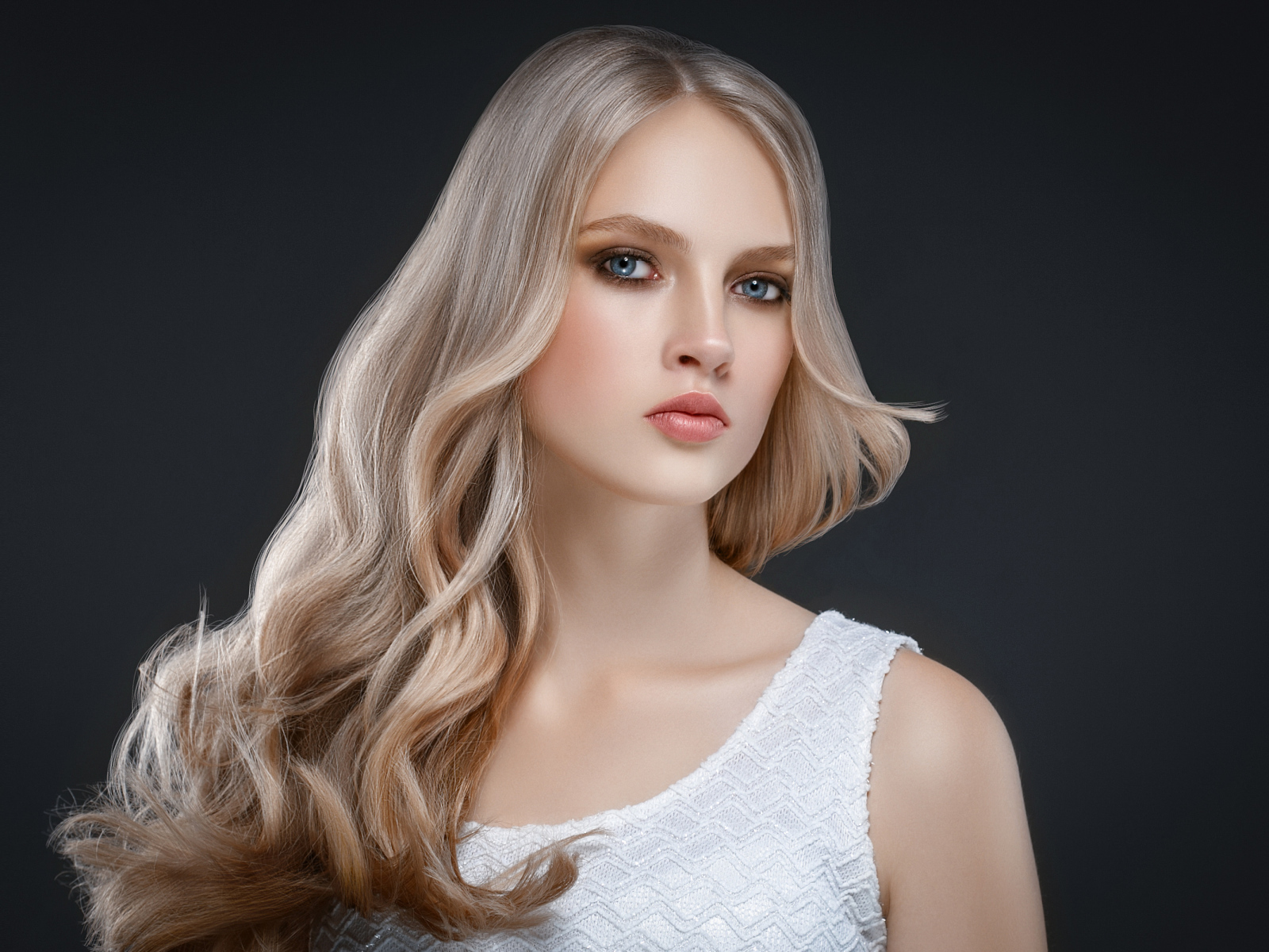 Красивая длинноволосая блондинка с голубыми глазами на сером фоне