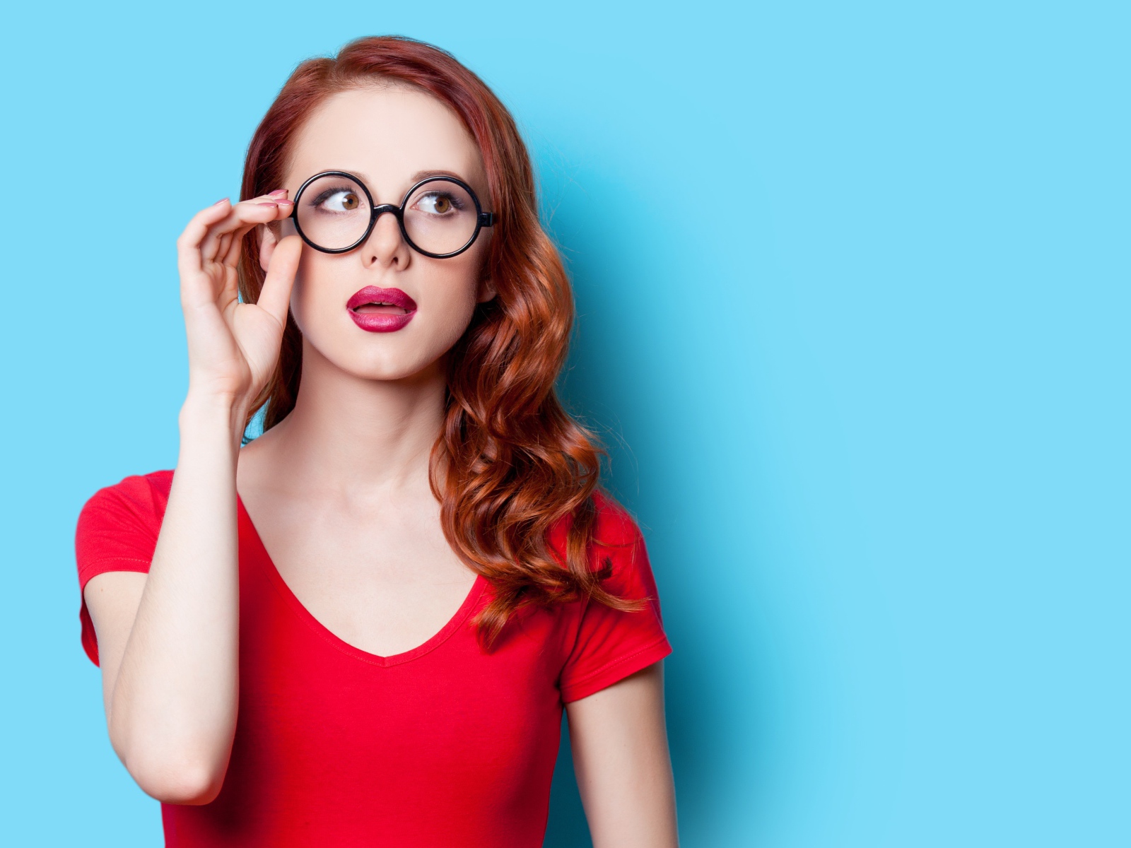 Красивая рыжеволосая девушка в очках на голубом фоне