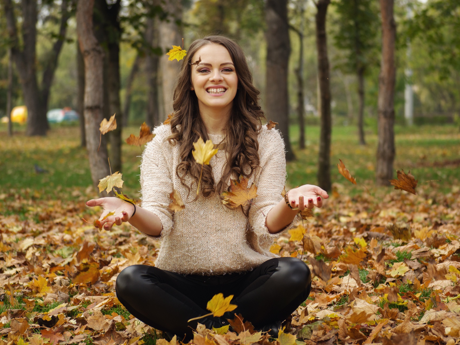 Красивая улыбающаяся девушка сидит на земле с желтыми листьями