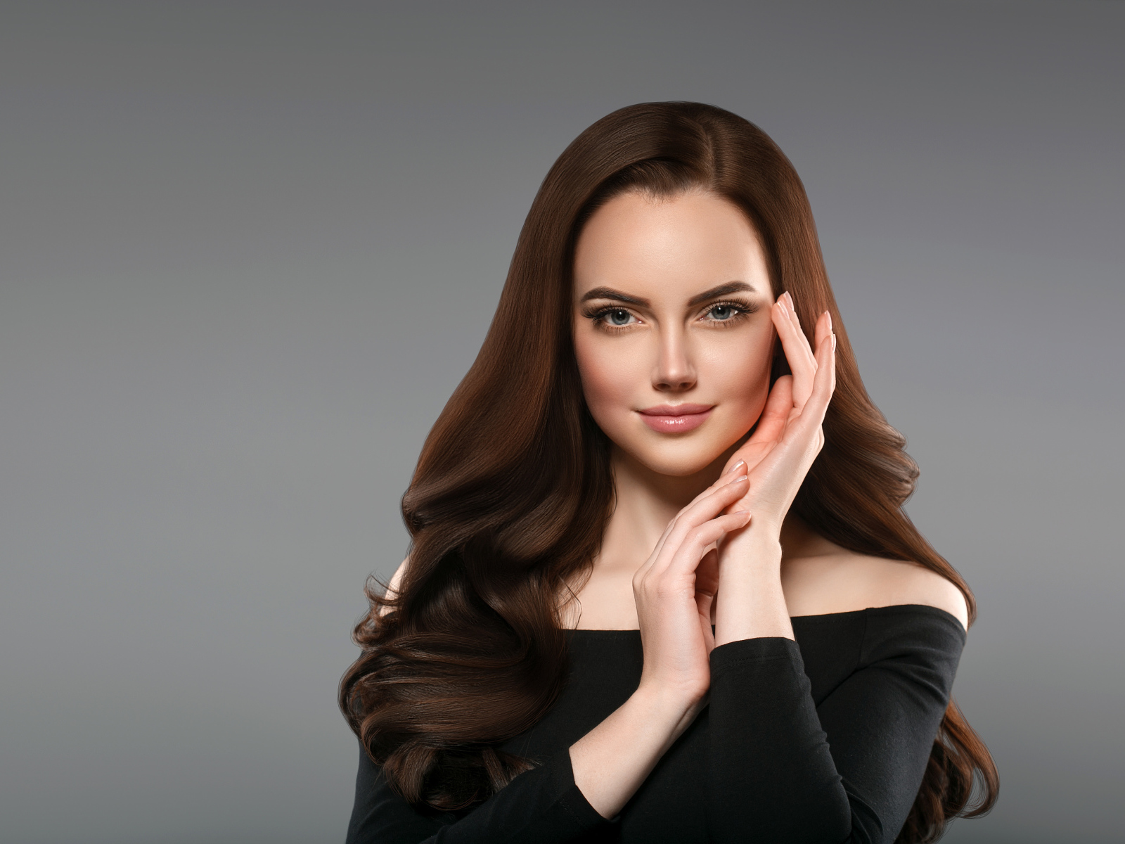 Красивая нежная длинноволосая шатенка  с руками у лица на сером фоне