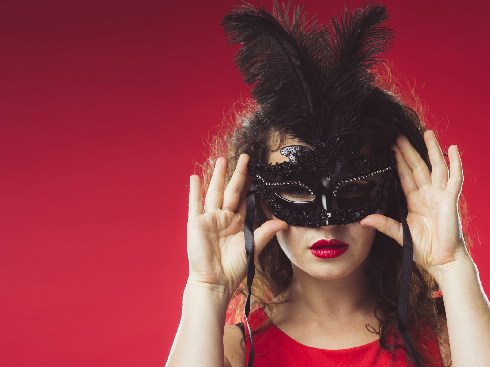 Красивая женщина в черной маске на красном фоне