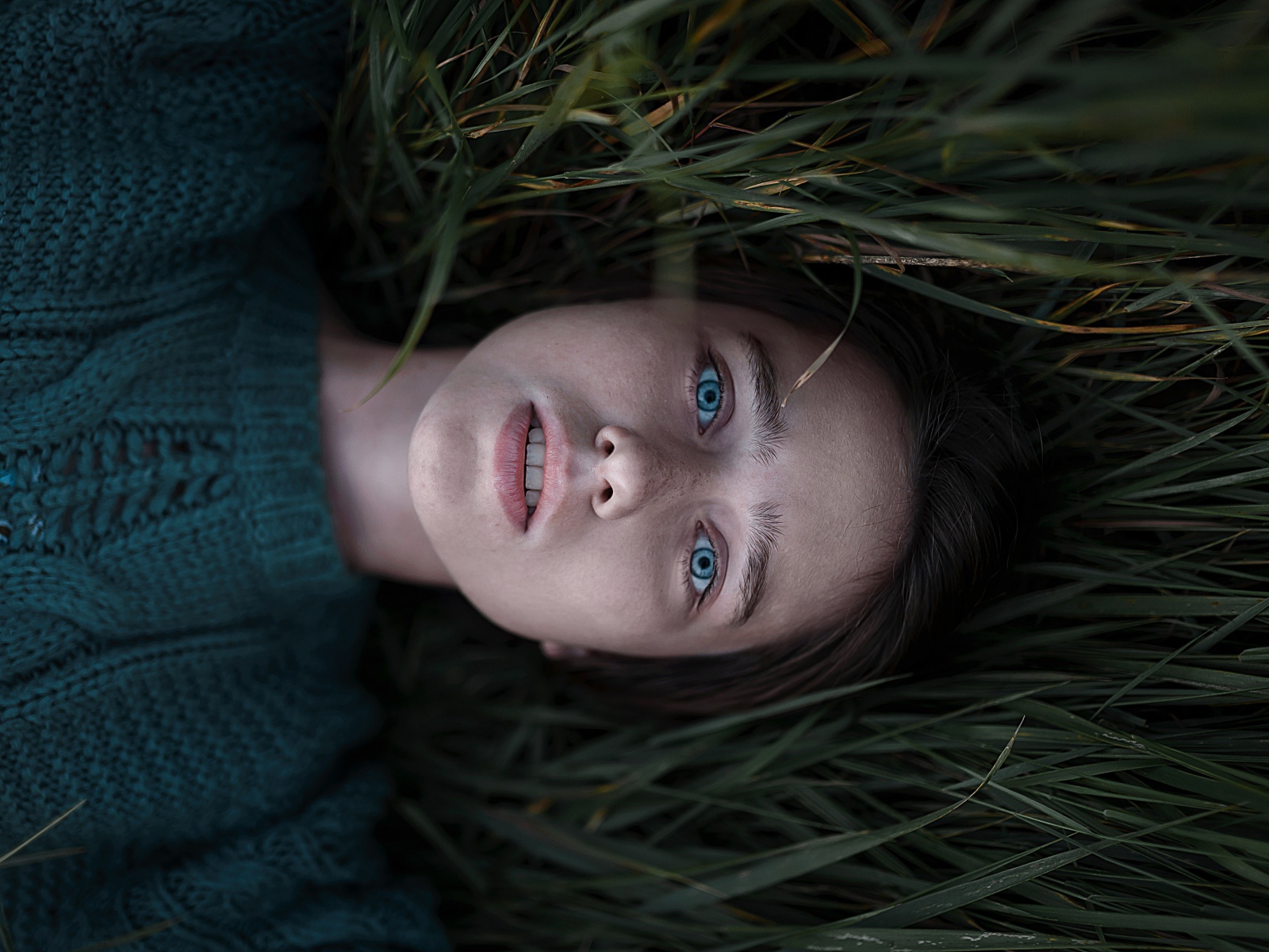 Голубоглазая девушка в свитере лежит на траве