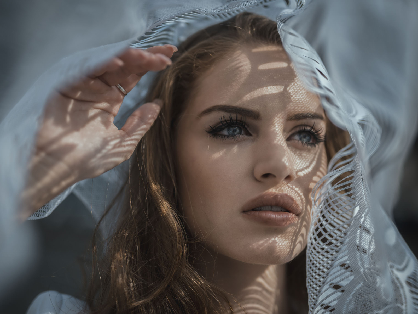 Голубоглазая девушка смотрит в окно с тюлью