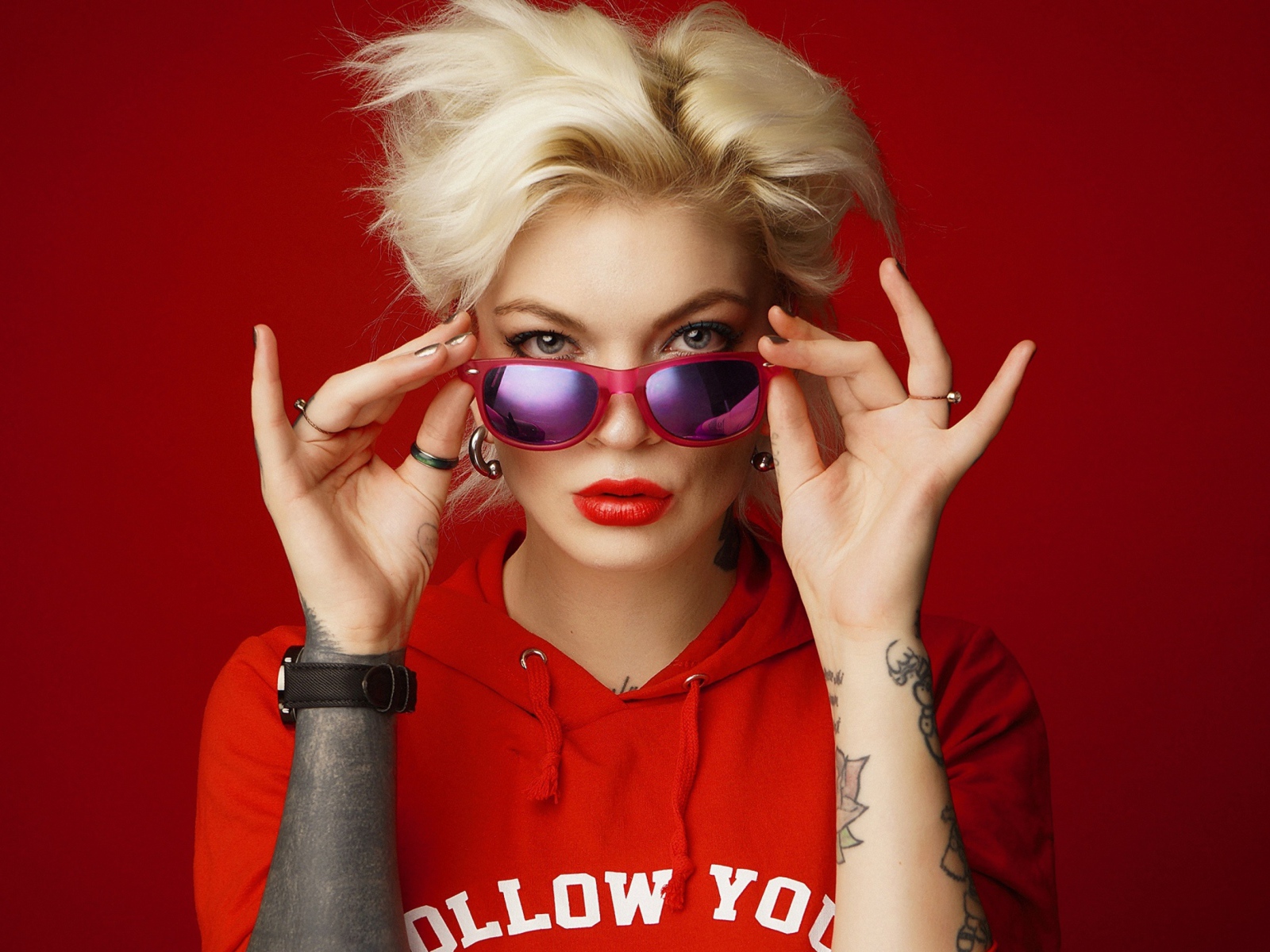 Яркая блондинка с татуировками на руках на красном фоне