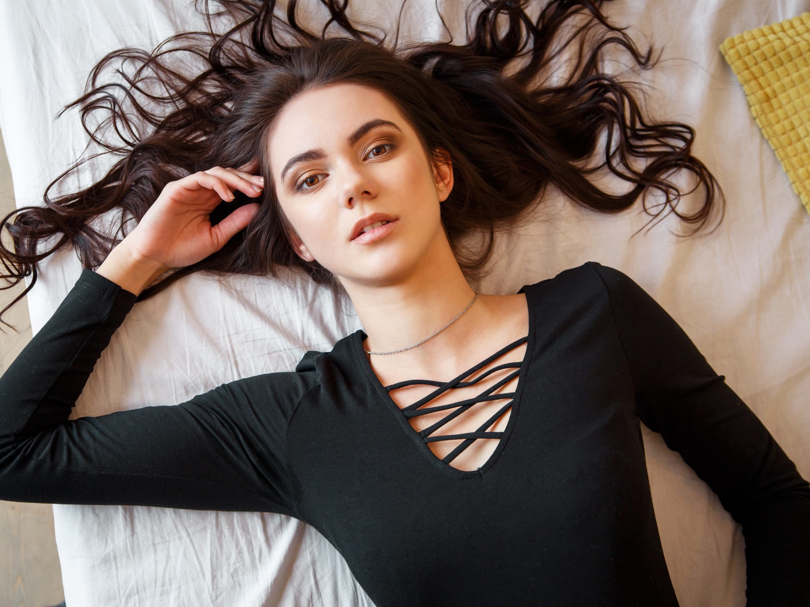 Кареглазая девушка в черном лежит на кровати