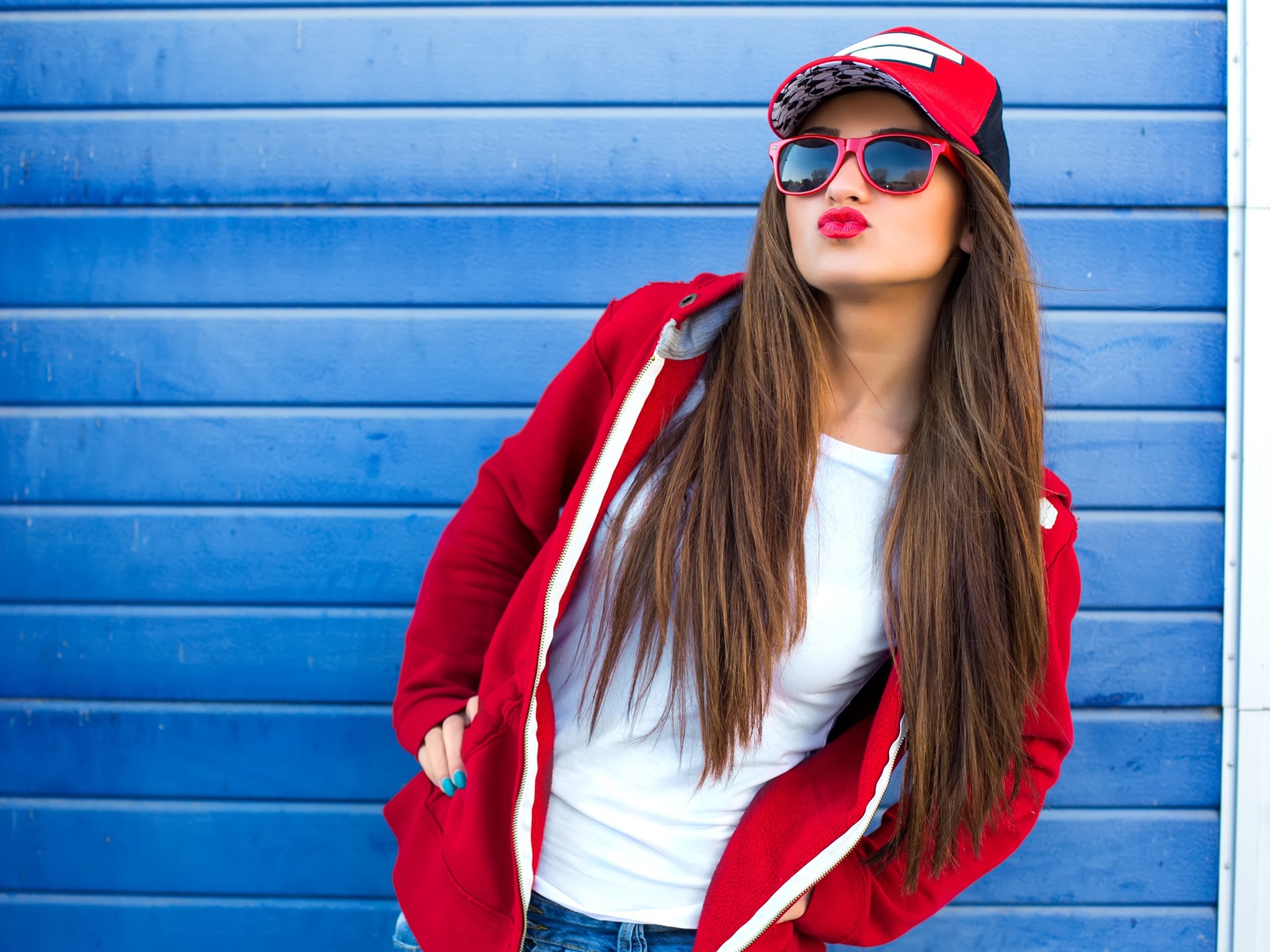 Девушка в бейсболке и солнечных очках у стены