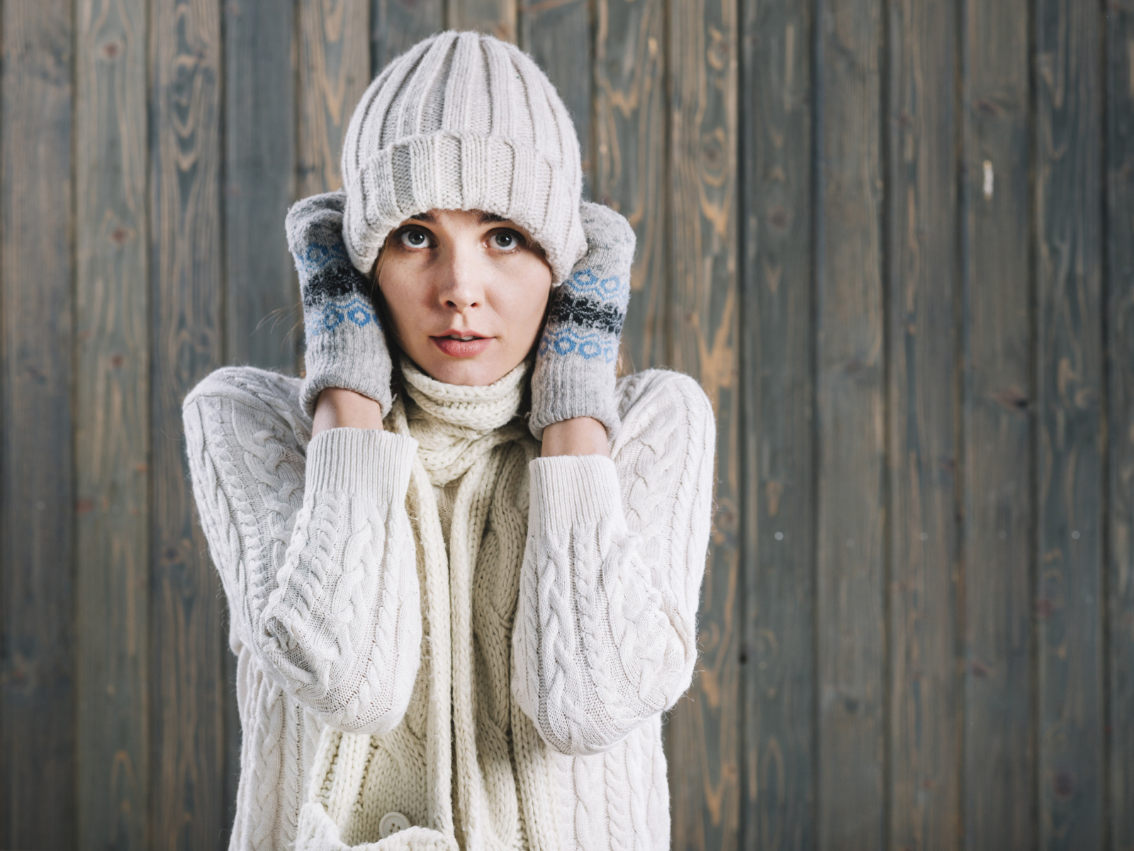 Девушка в варежках поправляет шапку на голове