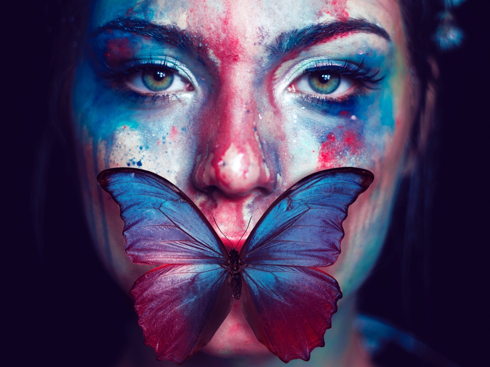 Лицо девушки в краске с бабочкой во рту