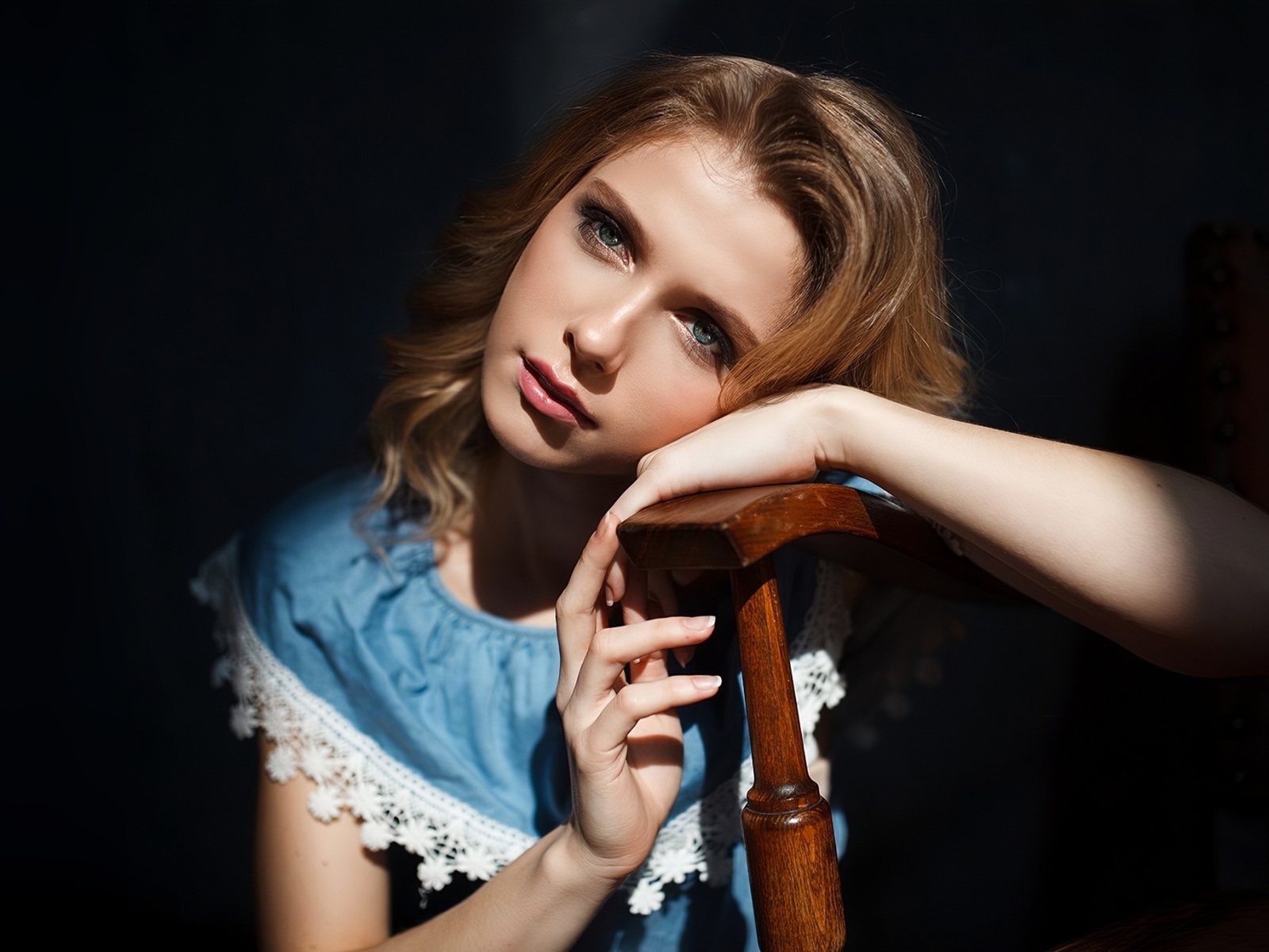 Грустная девушка сидит облокотившись об спинку кресла