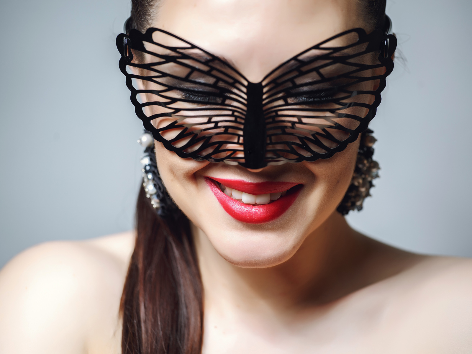 Улыбающаяся девушка в черной маске на сером фоне