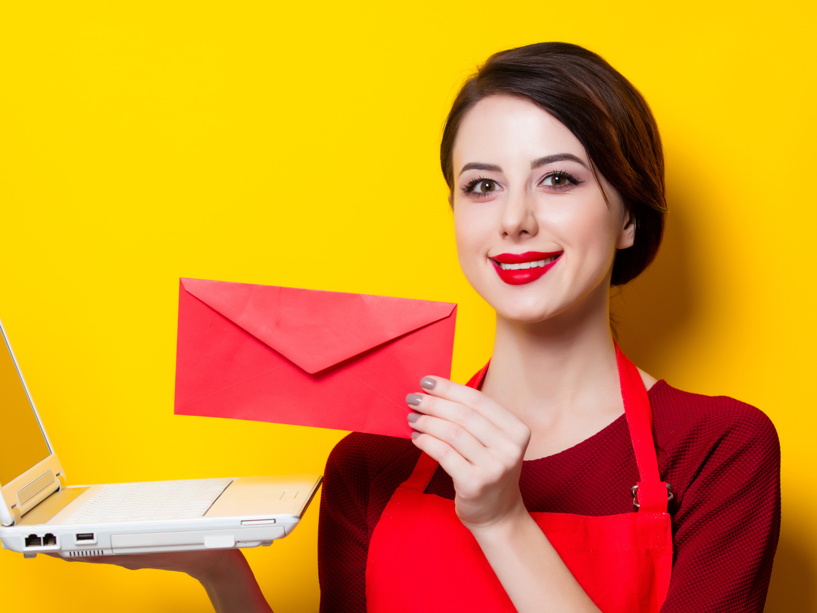 Улыбающаяся девушка с ноутбуком и конвертом в руках на желтом фоне
