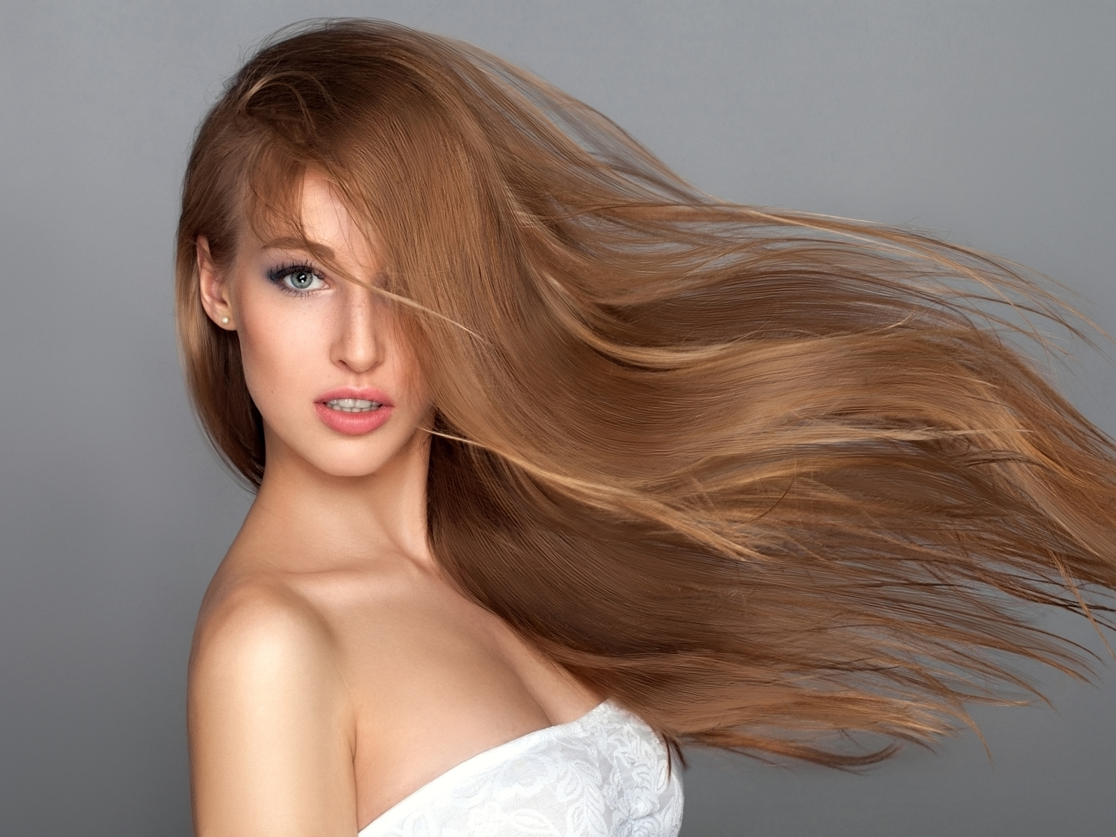 Ветер развивает волосы красивой девушки на сером фоне