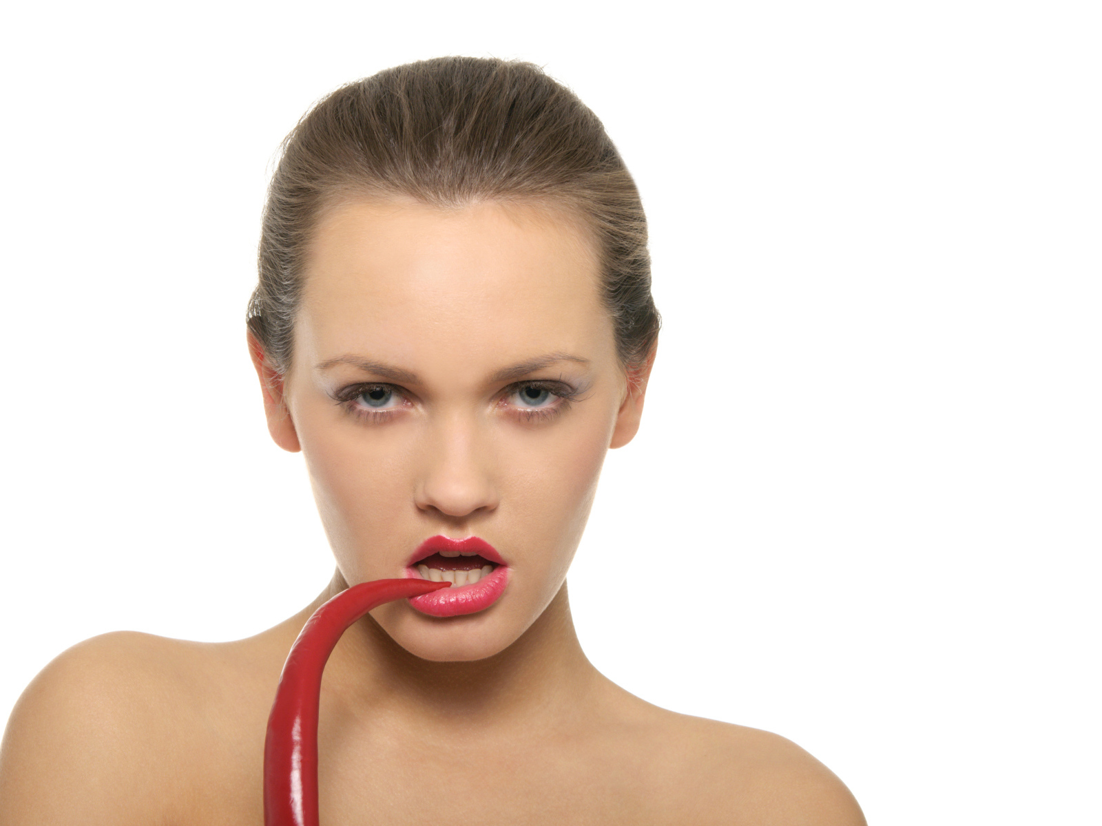 Молодая девушка кусает красный перец на белом фоне