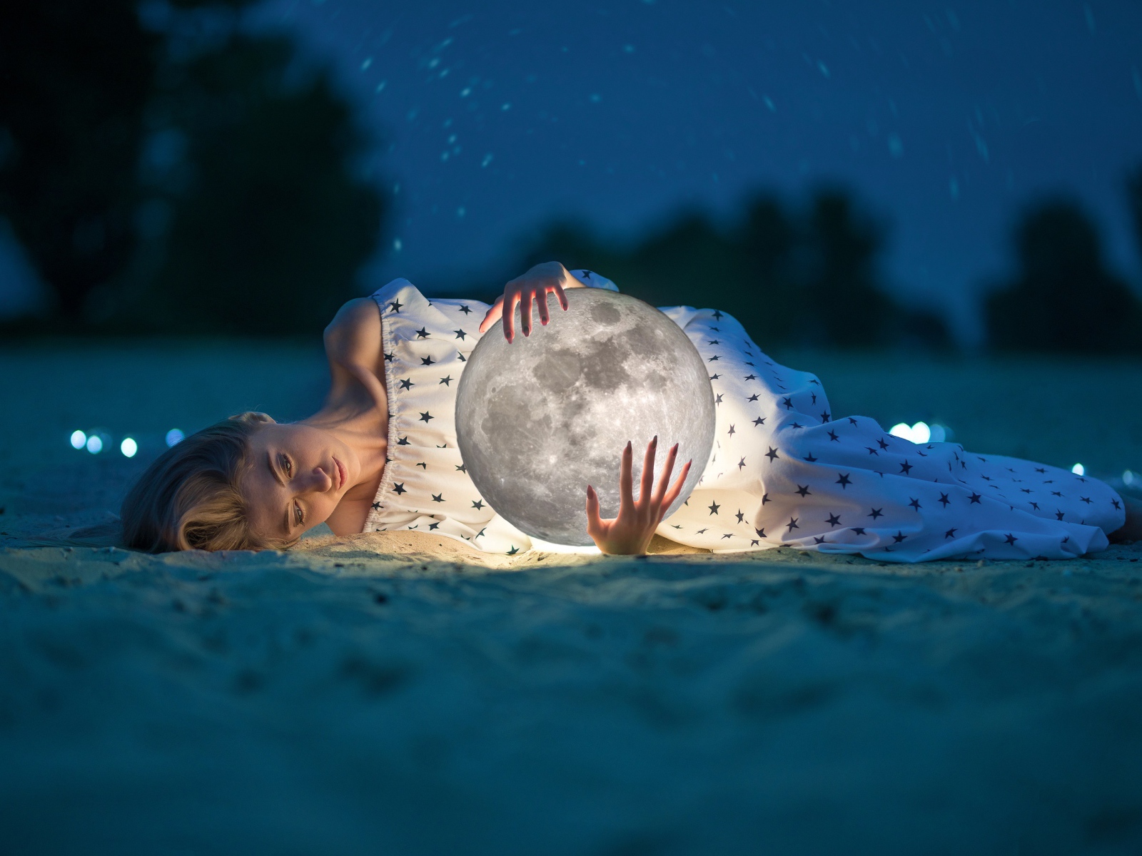 Молодая девушка с луной в руках лежит на песке