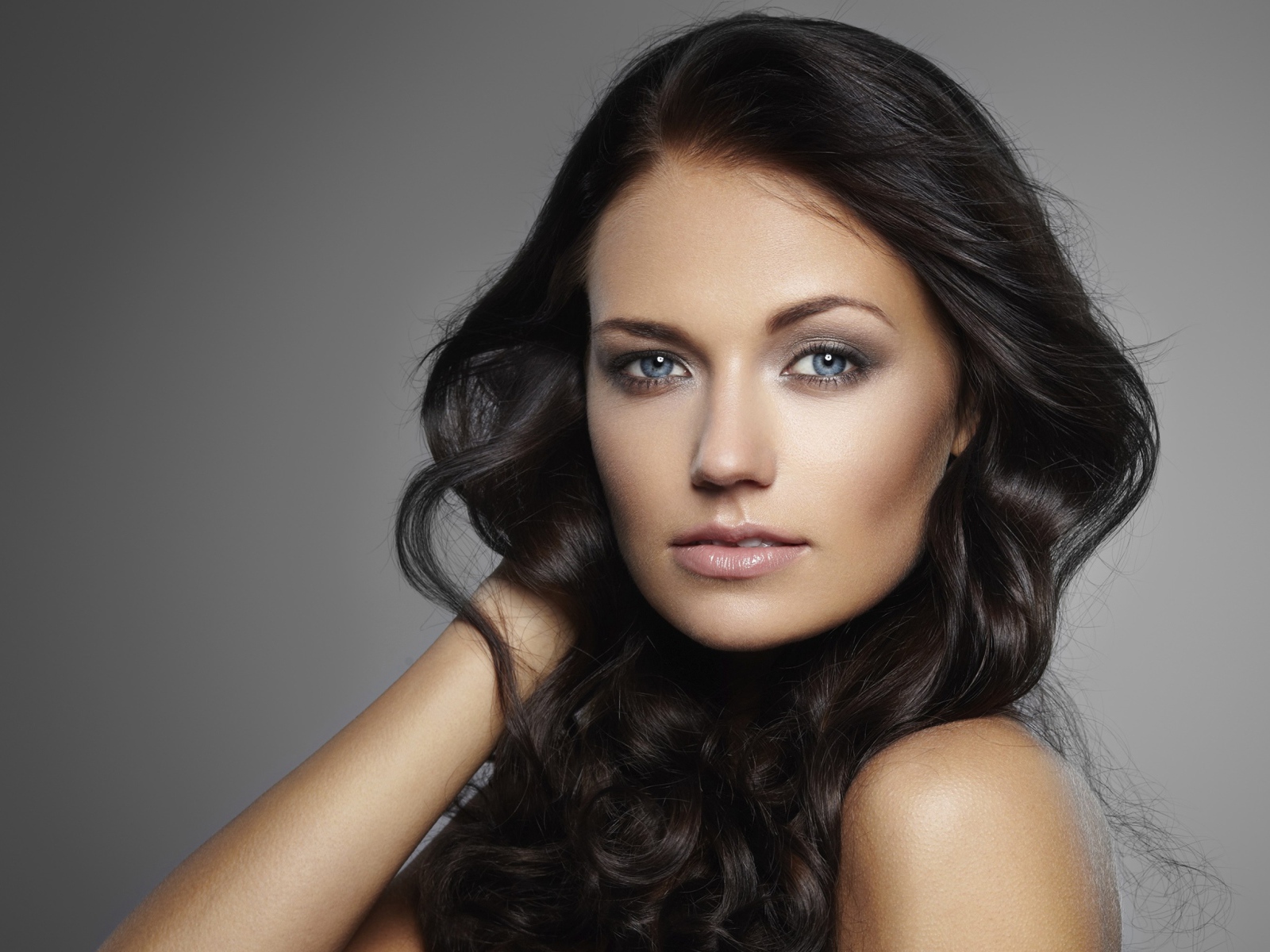 Молодая настоящая голубоглазая длинноволосая брюнетка на сером фоне