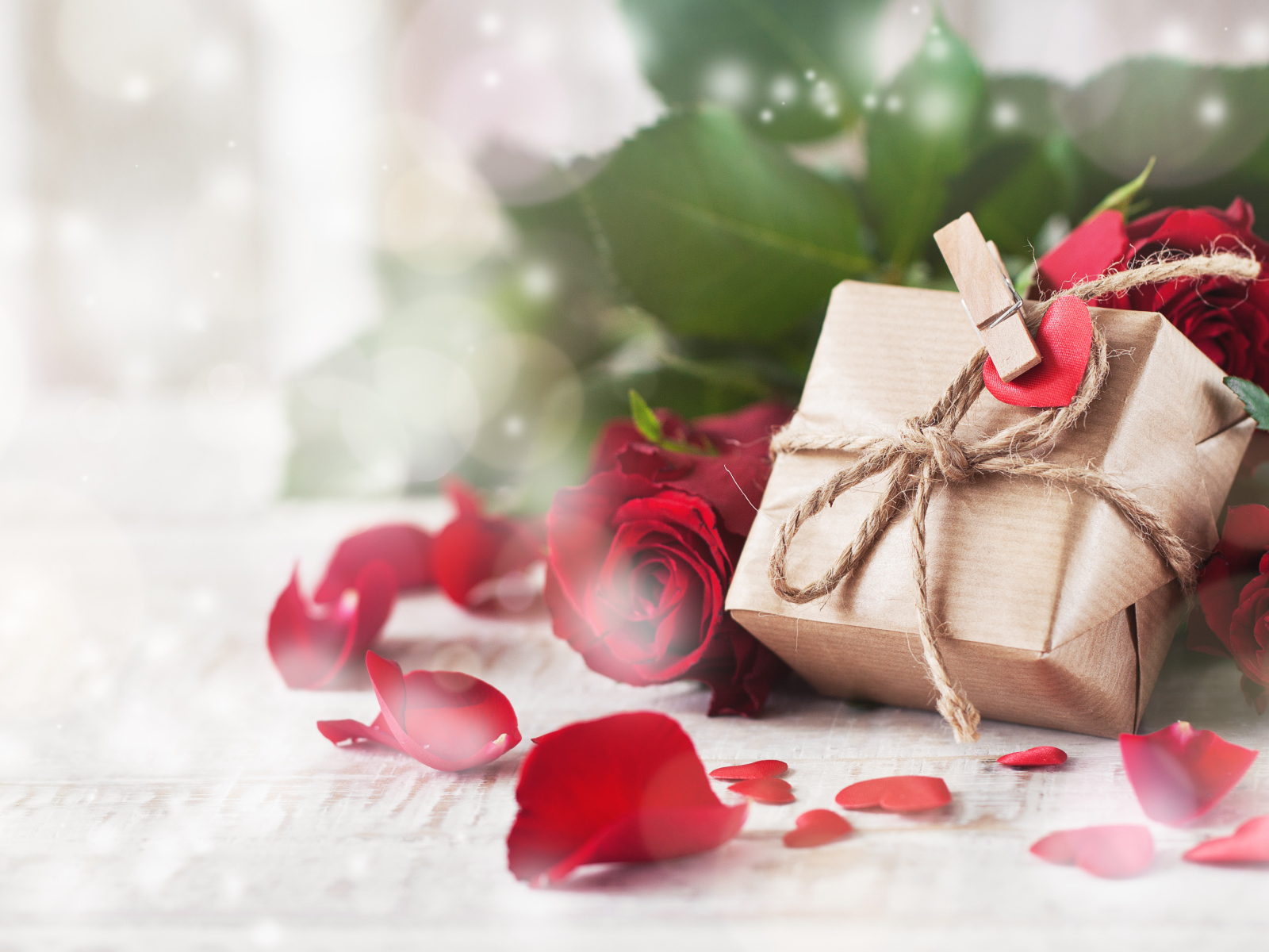 A gift in a box on a table with red roses