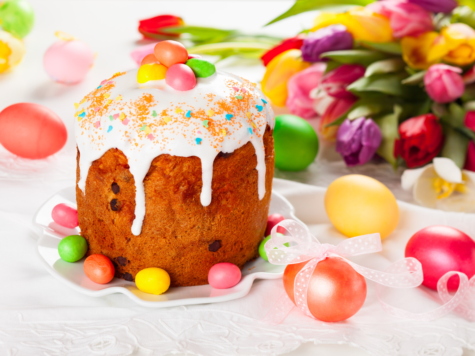 Красивый кулич с конфетами на столе с букетом тюльпанов и крашеными яйцами на Пасху