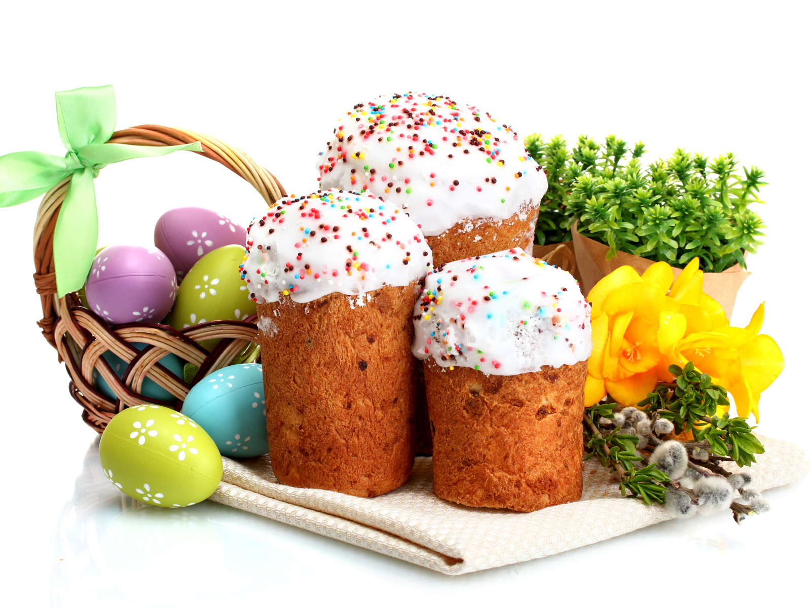 Три сладких кулича на белом фоне с цветами и крашеными яйцами к празднику Пасха