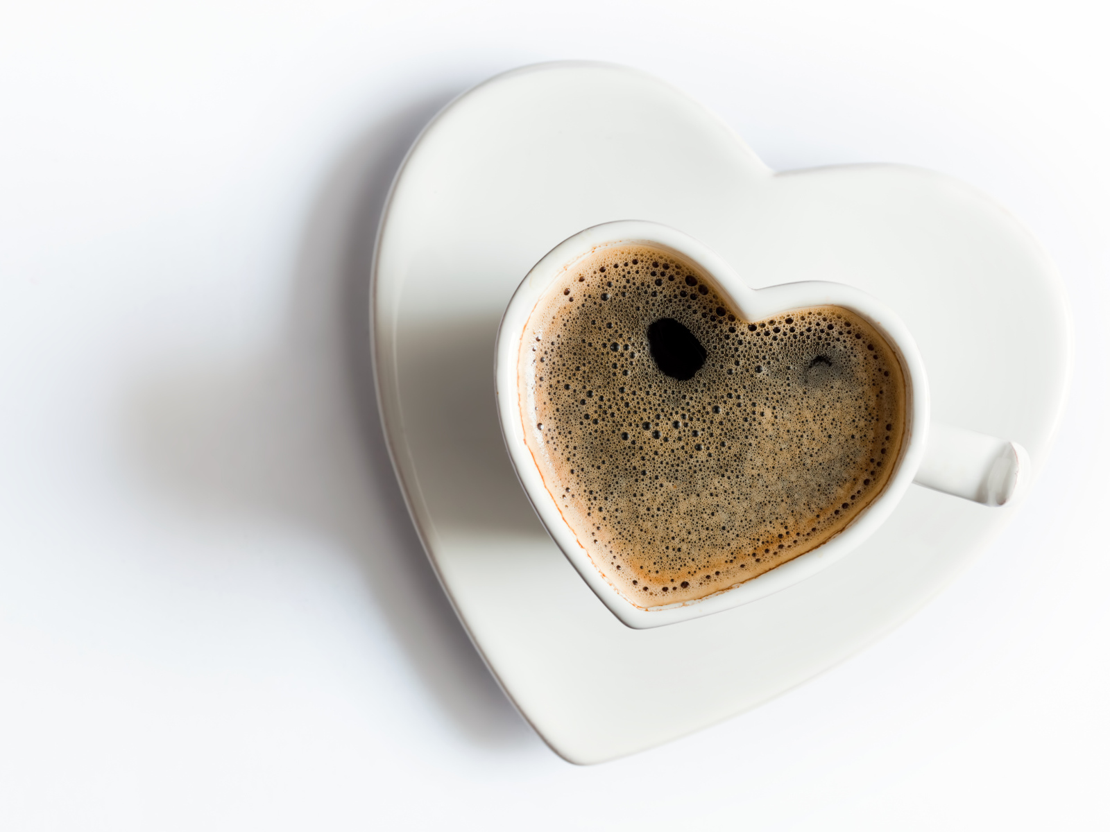 Красивая белая чашка в форме сердца с кофе на белом фоне