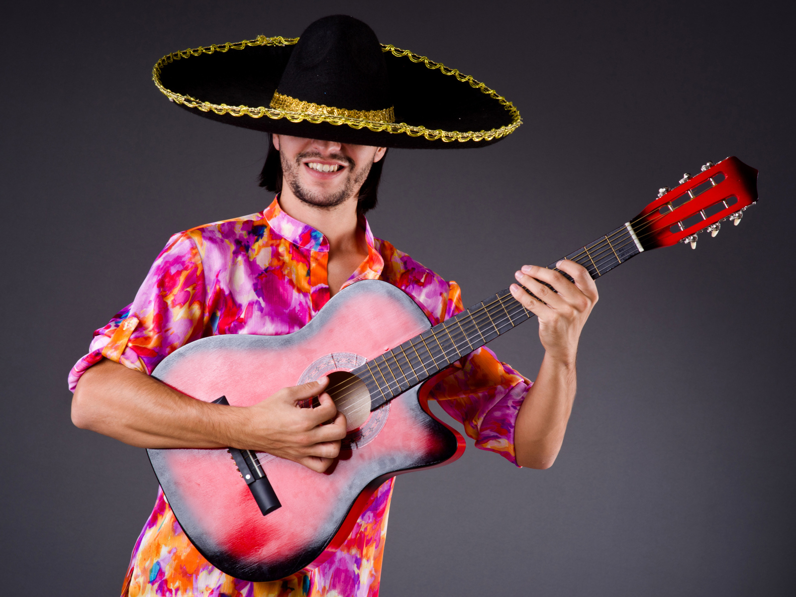Мужчина в сомбреро с гитарой в руках на сером фоне