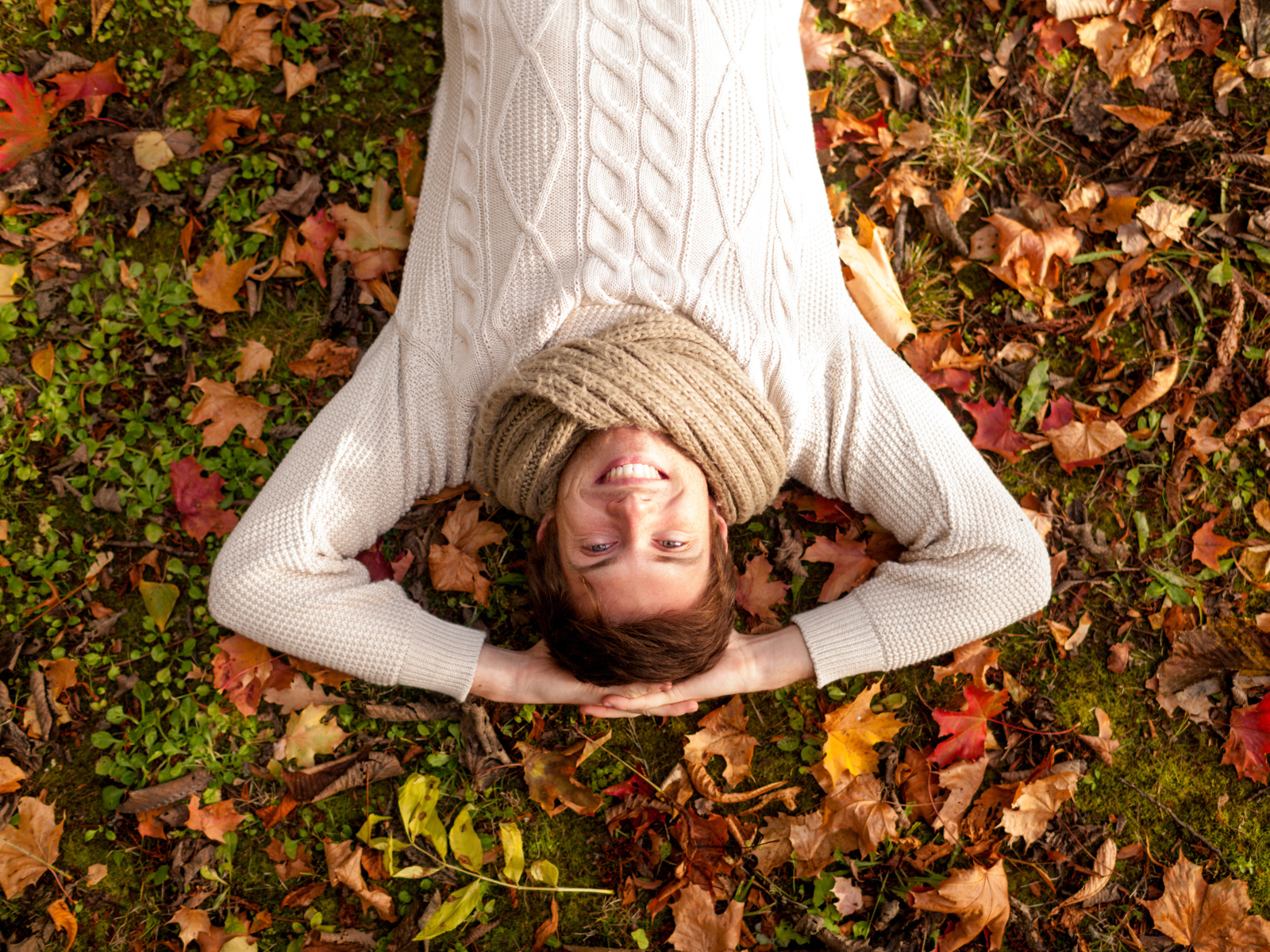 Улыбающийся мужчина в свитере лежит на опавших листьях 