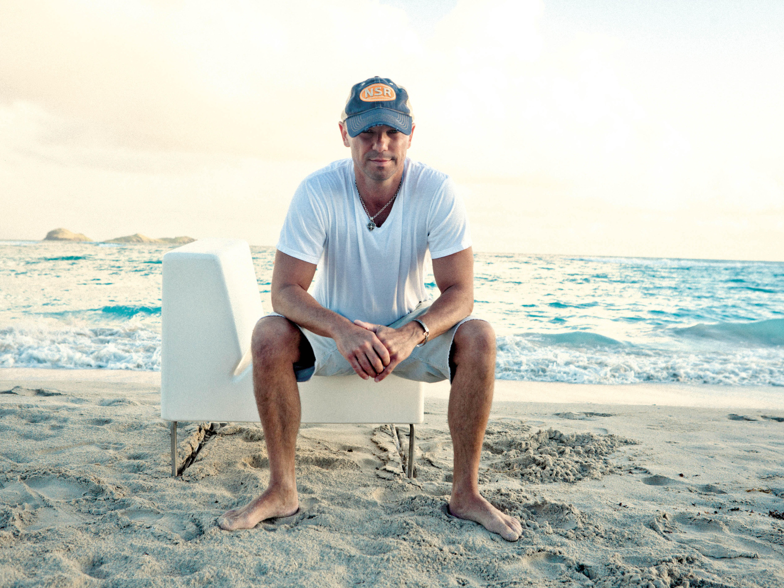 Исполнитель кантри Кенни Чесни на белом кресле на пляже