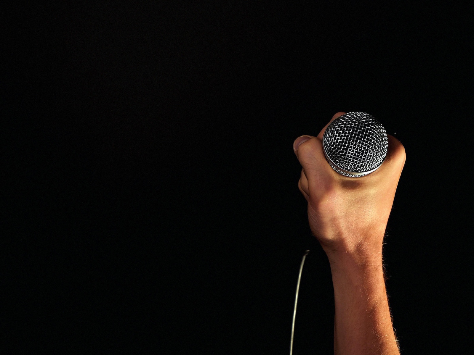 Микрофон в мужской руке на черном фоне