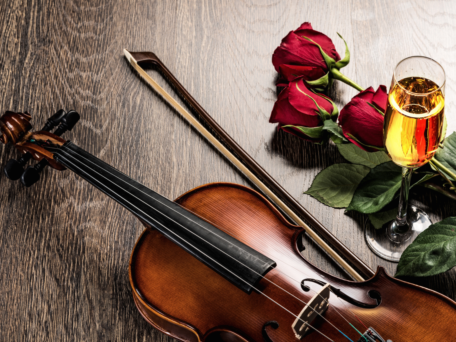 Скрипка лежит на столе с бокалом шампанского и красными розами