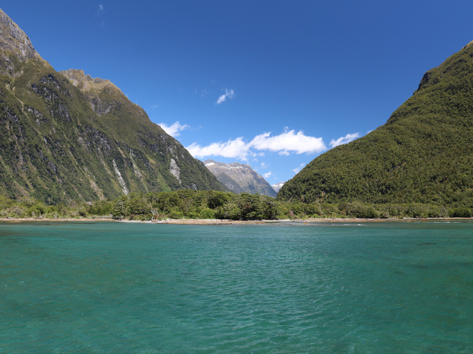 Голубая вода в озере на фоне покрытых зеленью гор под голубым небом