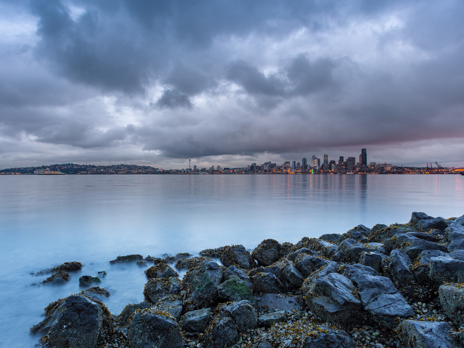 Камни на берегу реки на фоне города под пасмурным небом