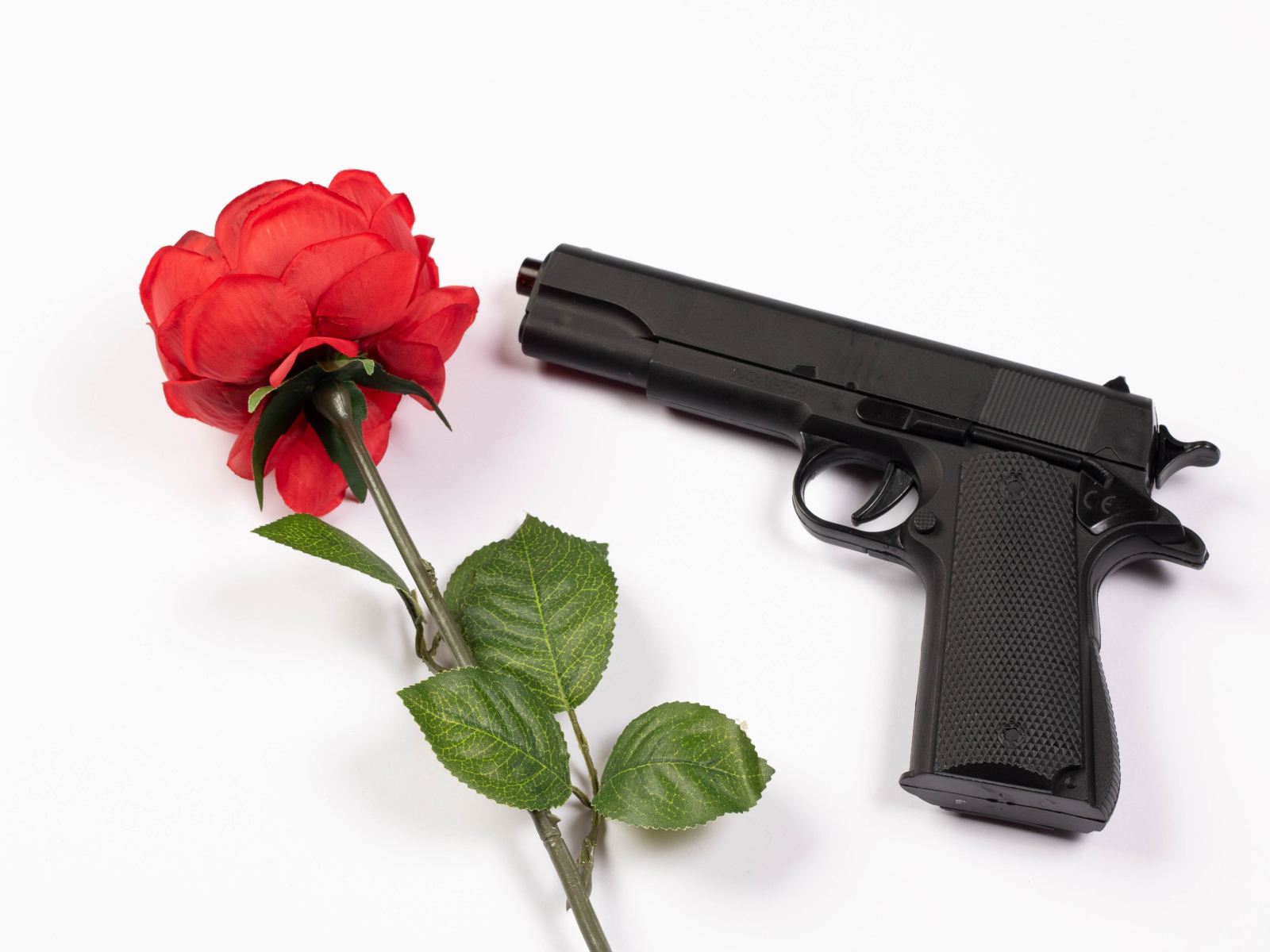 Красная роза и черный пистолет на белом фоне