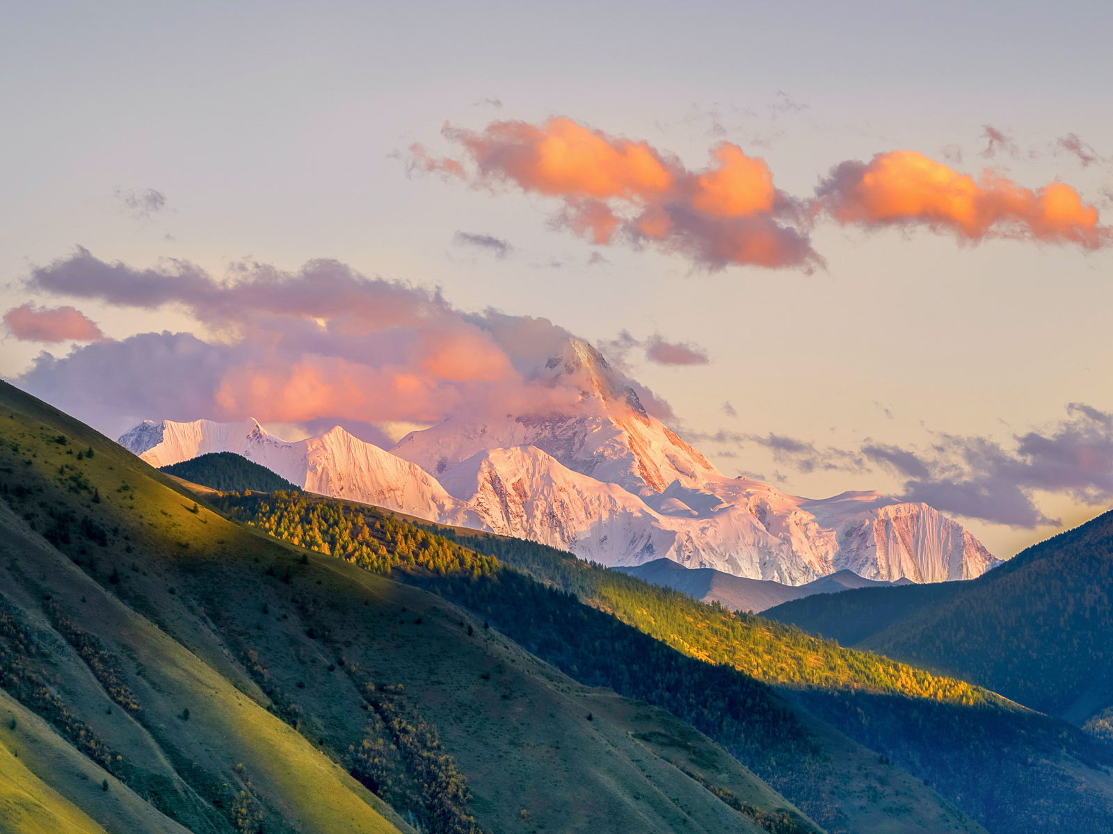 Заснеженные вершины гор у зеленых холмов под голубым небом